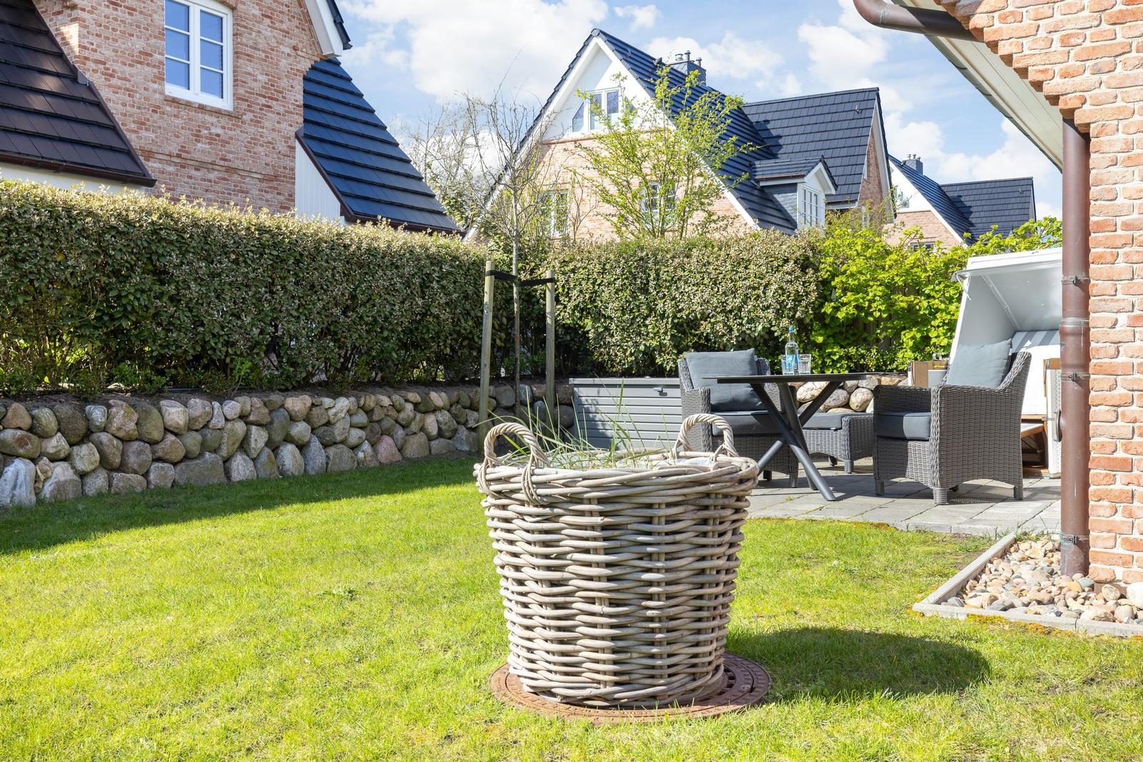Hinterhof mit Garten, Sitzgelegenheit und Korb. Steinmauer und Hecke im Hintergrund.
