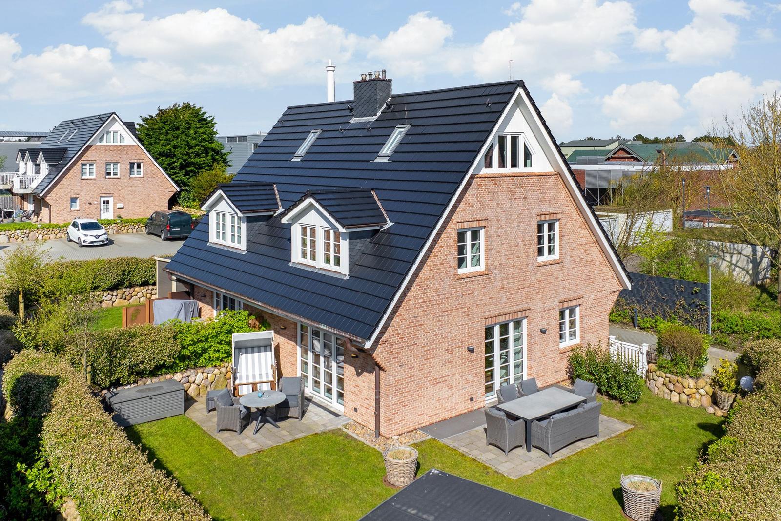 Haus mit Terrasse, Garten und Grillplatz. Schwarze Dachziegel und rote Ziegelmauer.