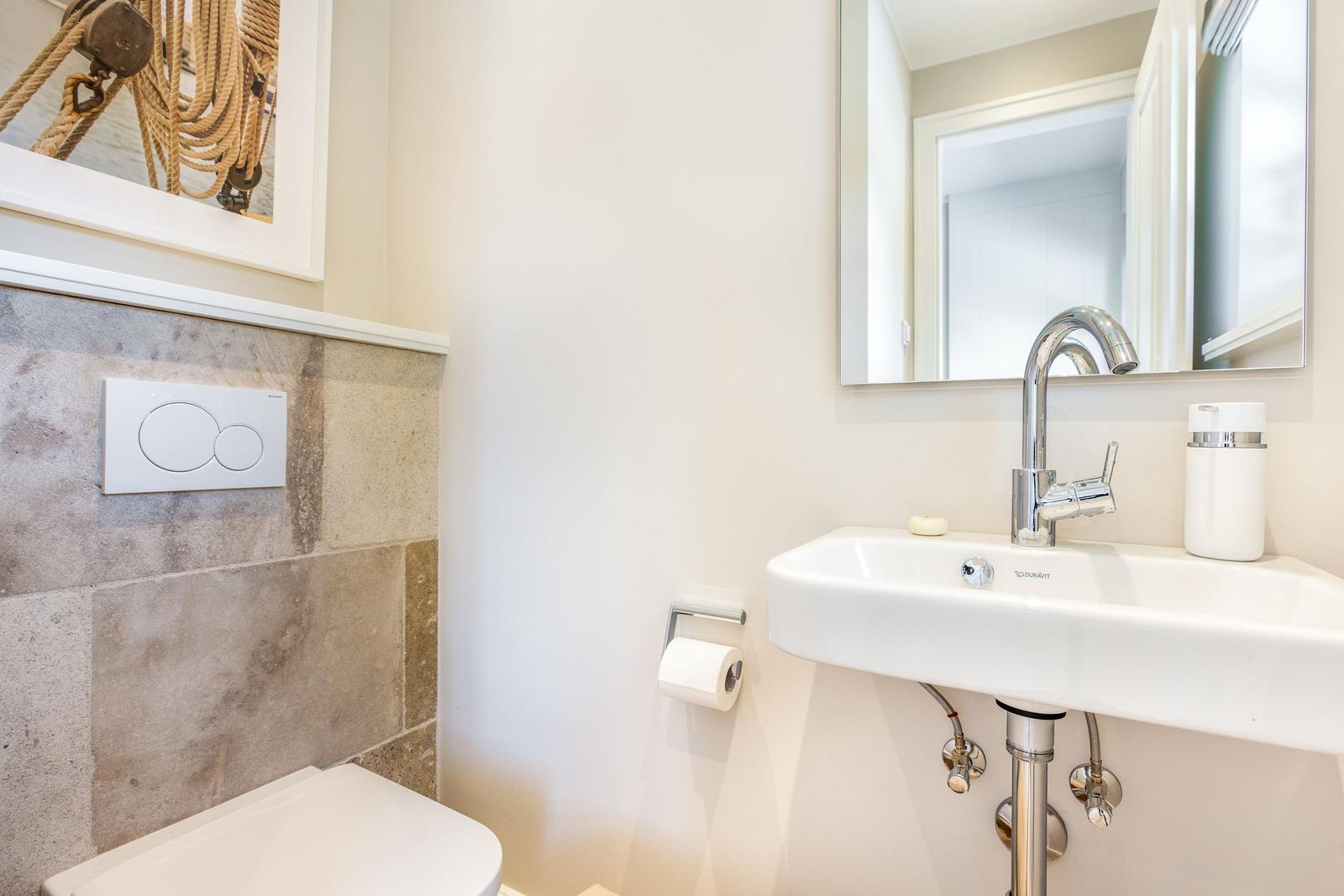 Badezimmer mit Waschbecken, Spiegel und Toilette. Wand mit Steinfliesen und Kunstwerk.