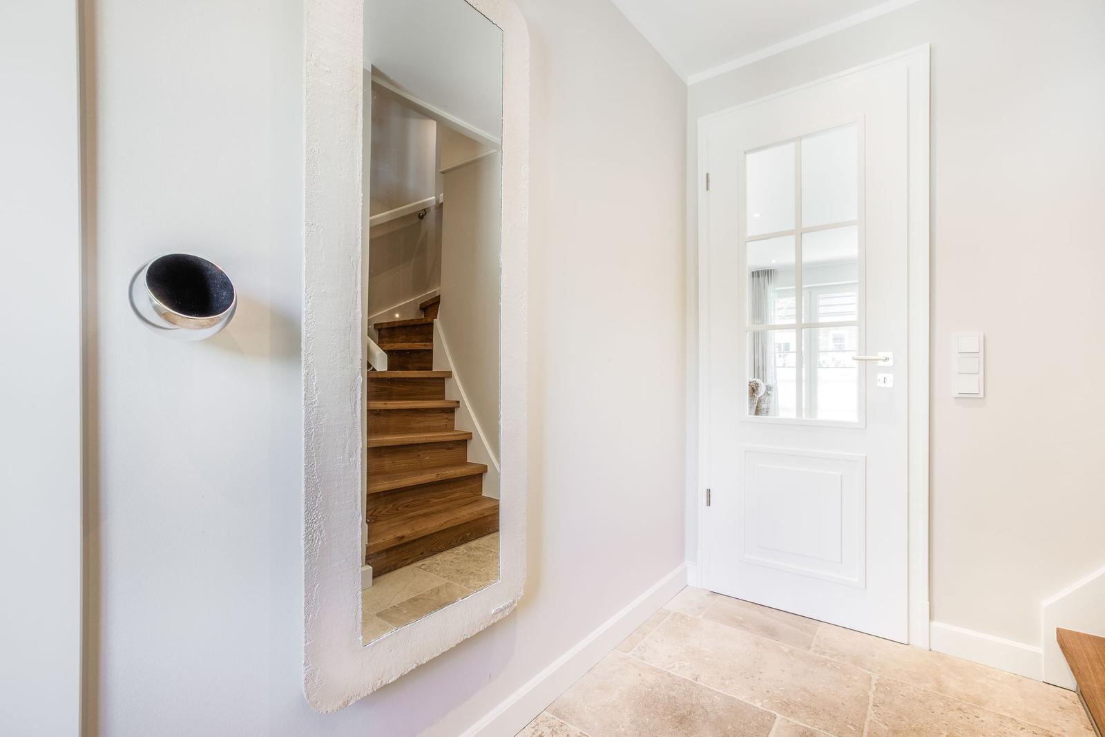 Hausflur mit Spiegel, Holztreppe und weiße Tür mit Glasfenstern.