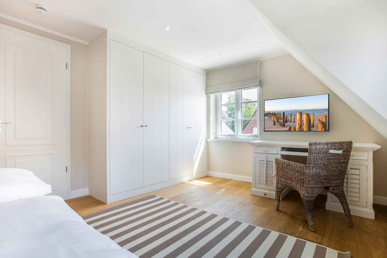 Schlafzimmer mit weißem Schrank, Schreibtisch und TV unter Dachschräge.