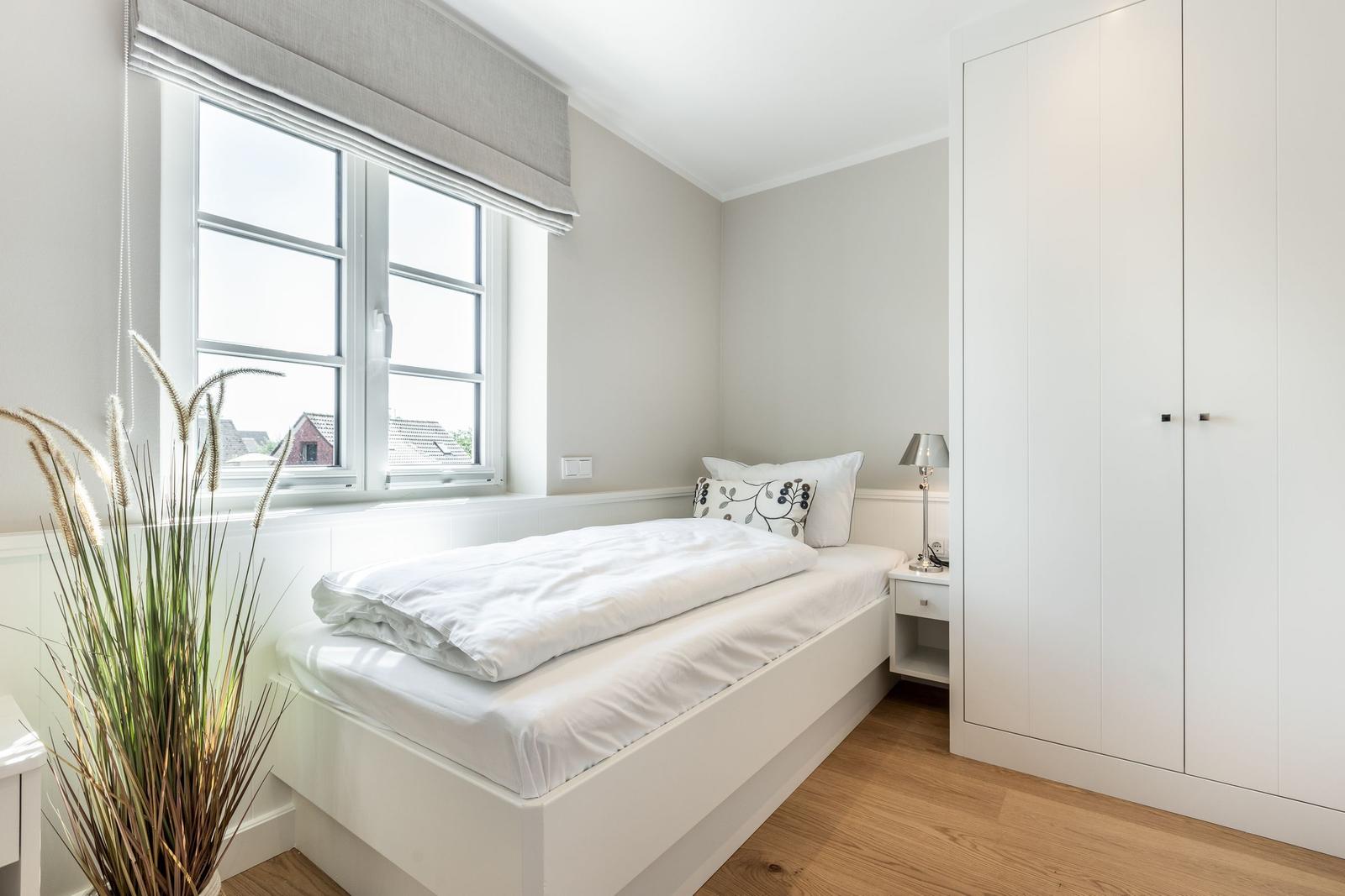 Schlafzimmer mit weißem Bett, Kleiderschrank und Fenster mit Blick auf Dächer.