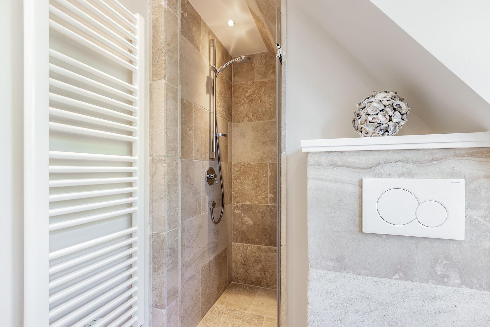 Dusche mit Steinwand, Heizkörper und WC mit Schalter.