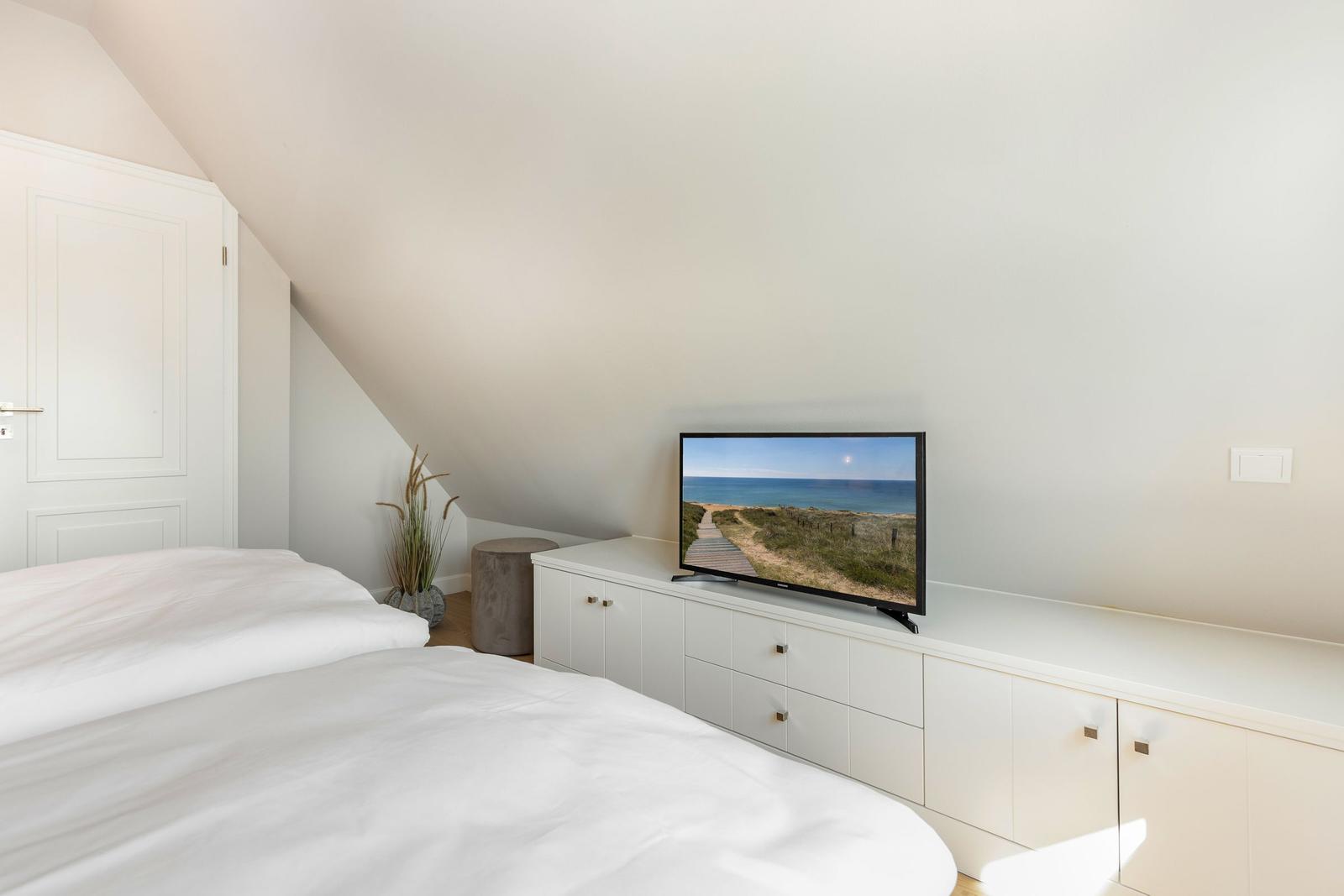 Schlafzimmer mit Dachschrägen, Bett, TV und Schrank.