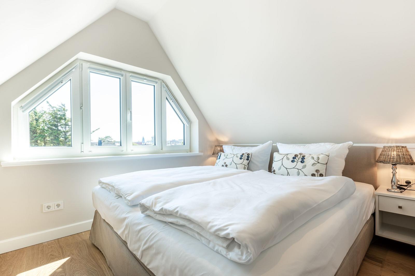 Doppelbett mit weißen Bettwäsche und Fenster mit Blick.