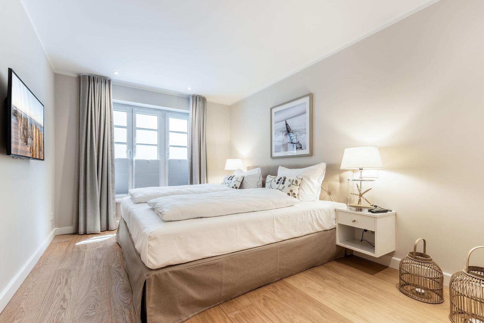 Schlafzimmer mit Doppelbett, TV und Fenster mit Vorhängen.