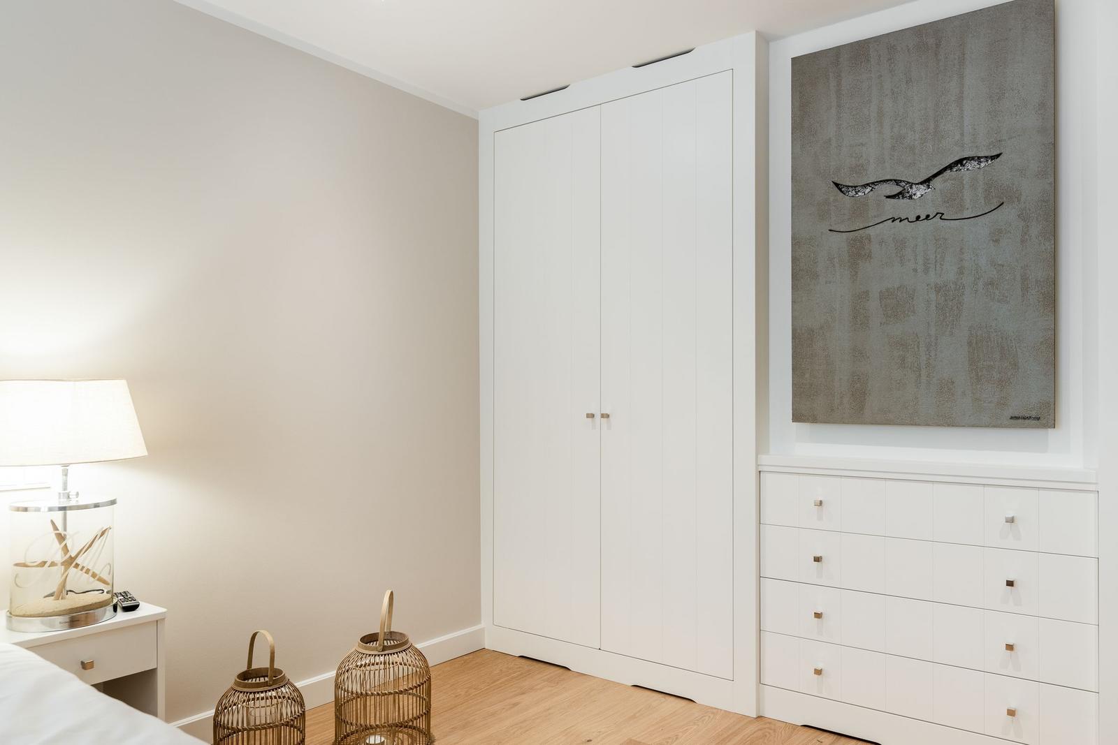 Schlafzimmer mit weißem Schrank, Kommode und Wandbild mit Vogel.