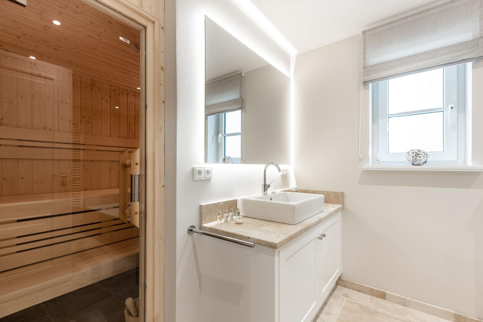 Badezimmer mit Waschbecken, Spiegel und Sauna im Hintergrund.