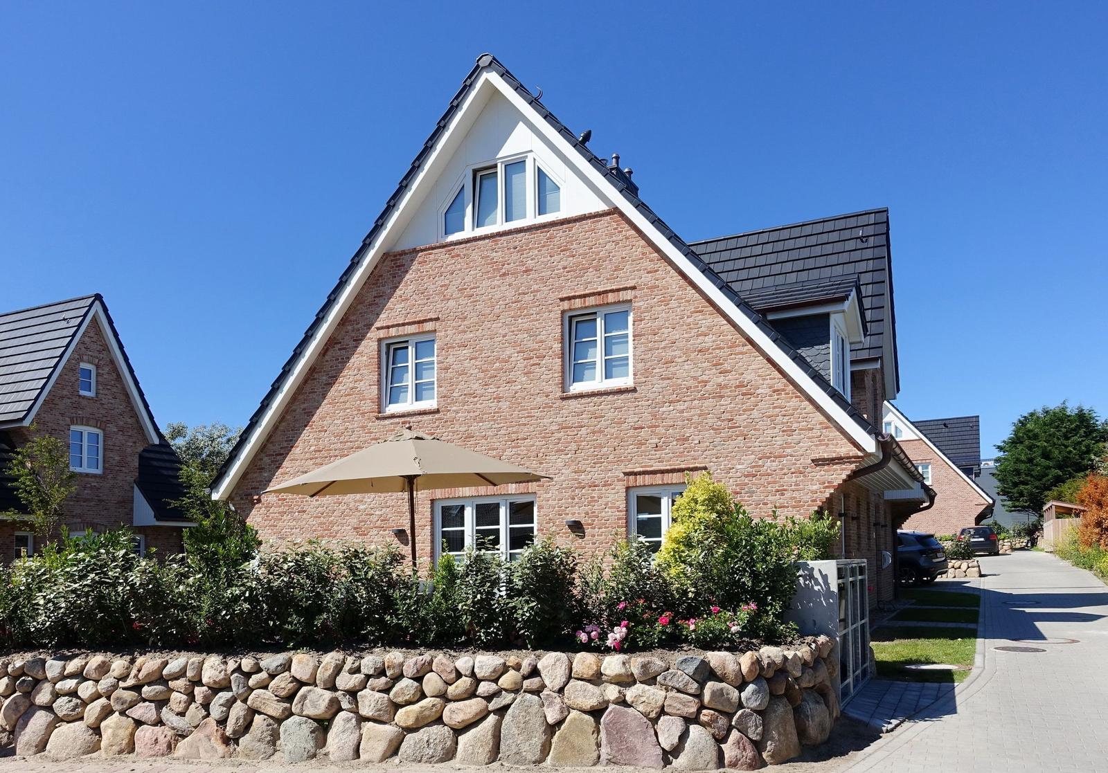 Zweistöckiges Haus mit Steinmauer und Terrasse unter Sonnenschirm.