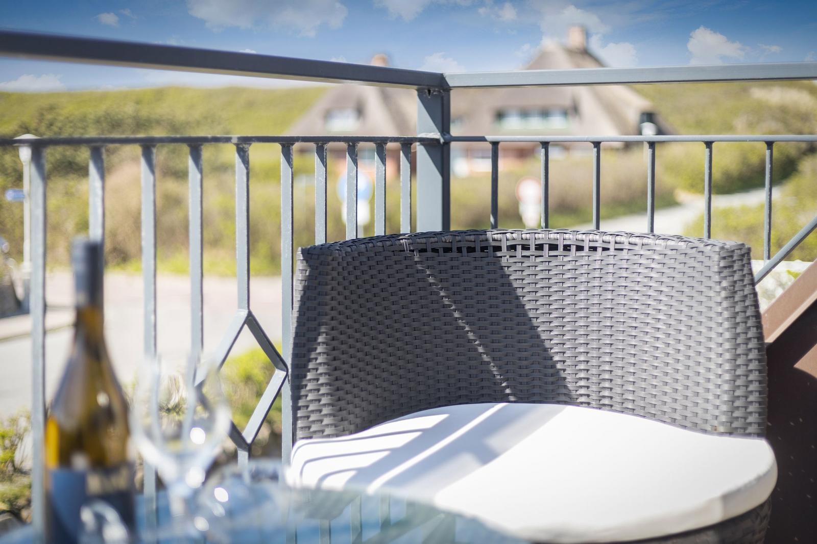 Terrace with chair and table, view of green landscape and house in the background.