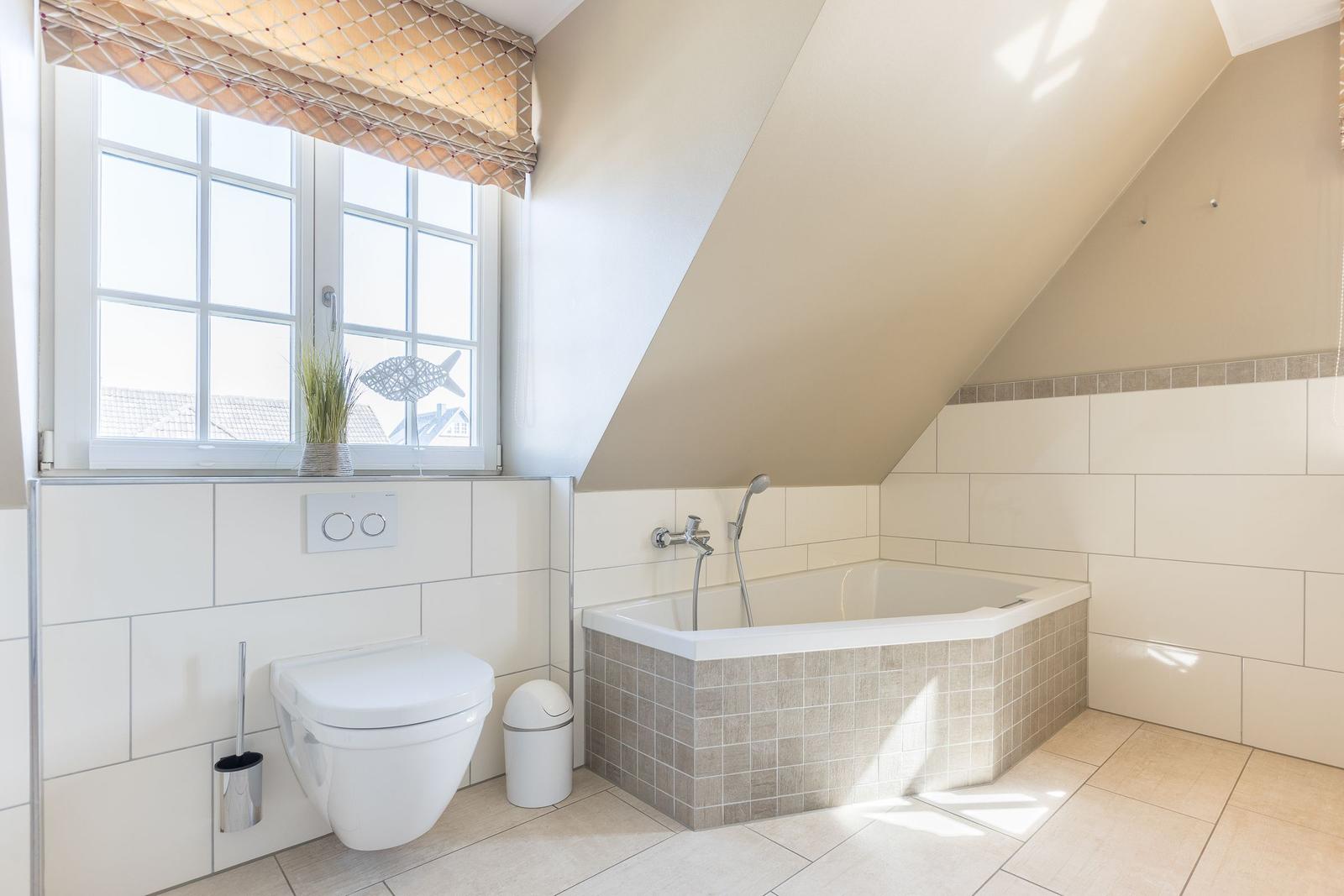 Bathroom with bathtub, toilet, and window with roller blind.