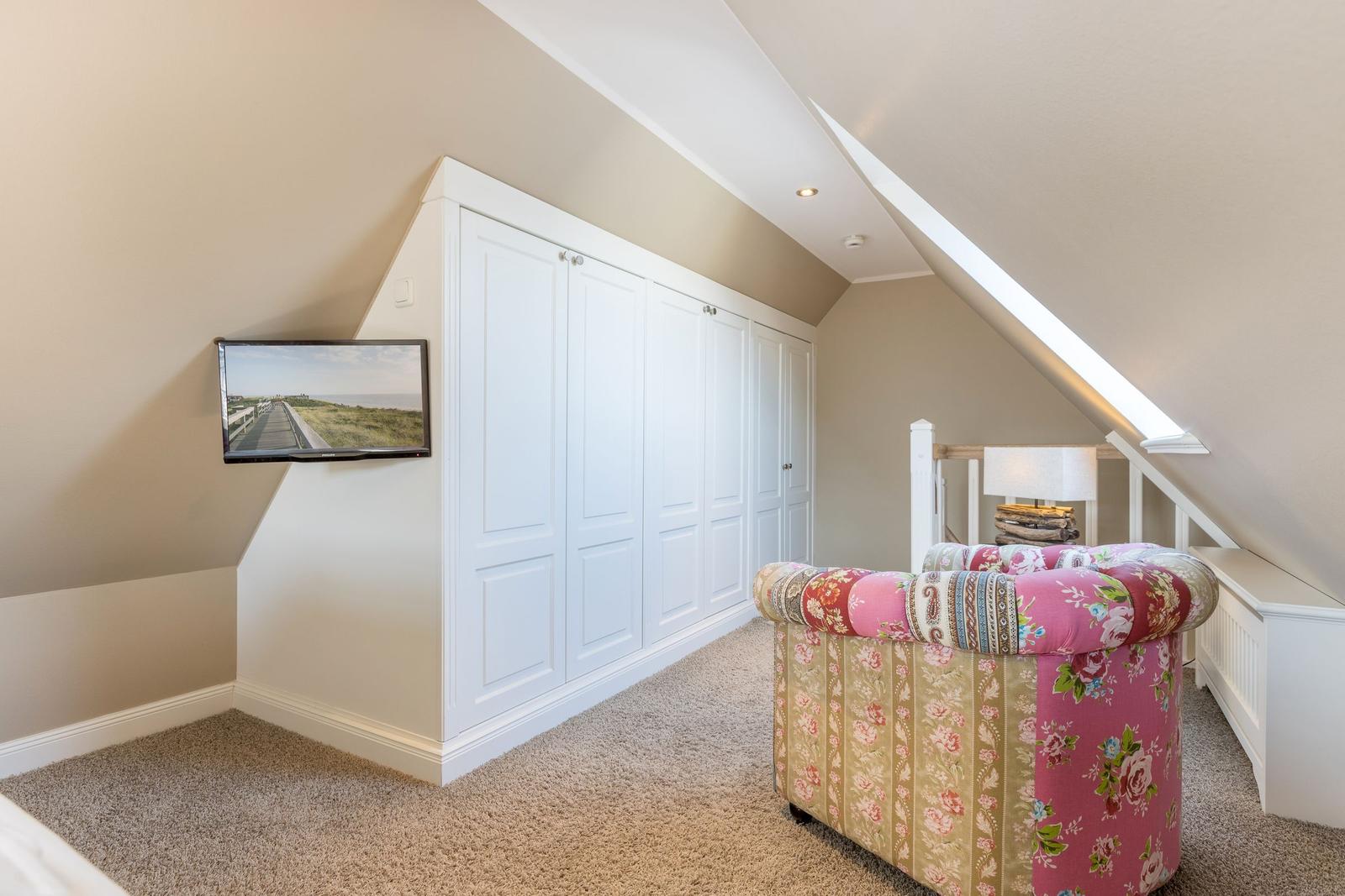 Bedroom with sloped ceiling, white closet, and patterned armchair.