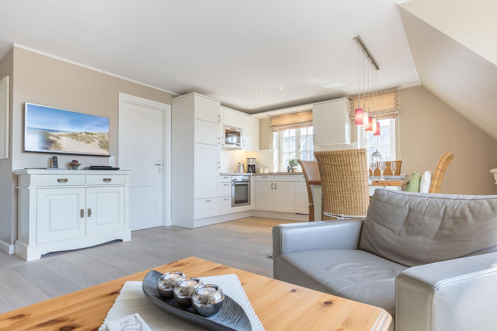 Living and kitchen area with sofa, TV, and dining table under a sloped ceiling.