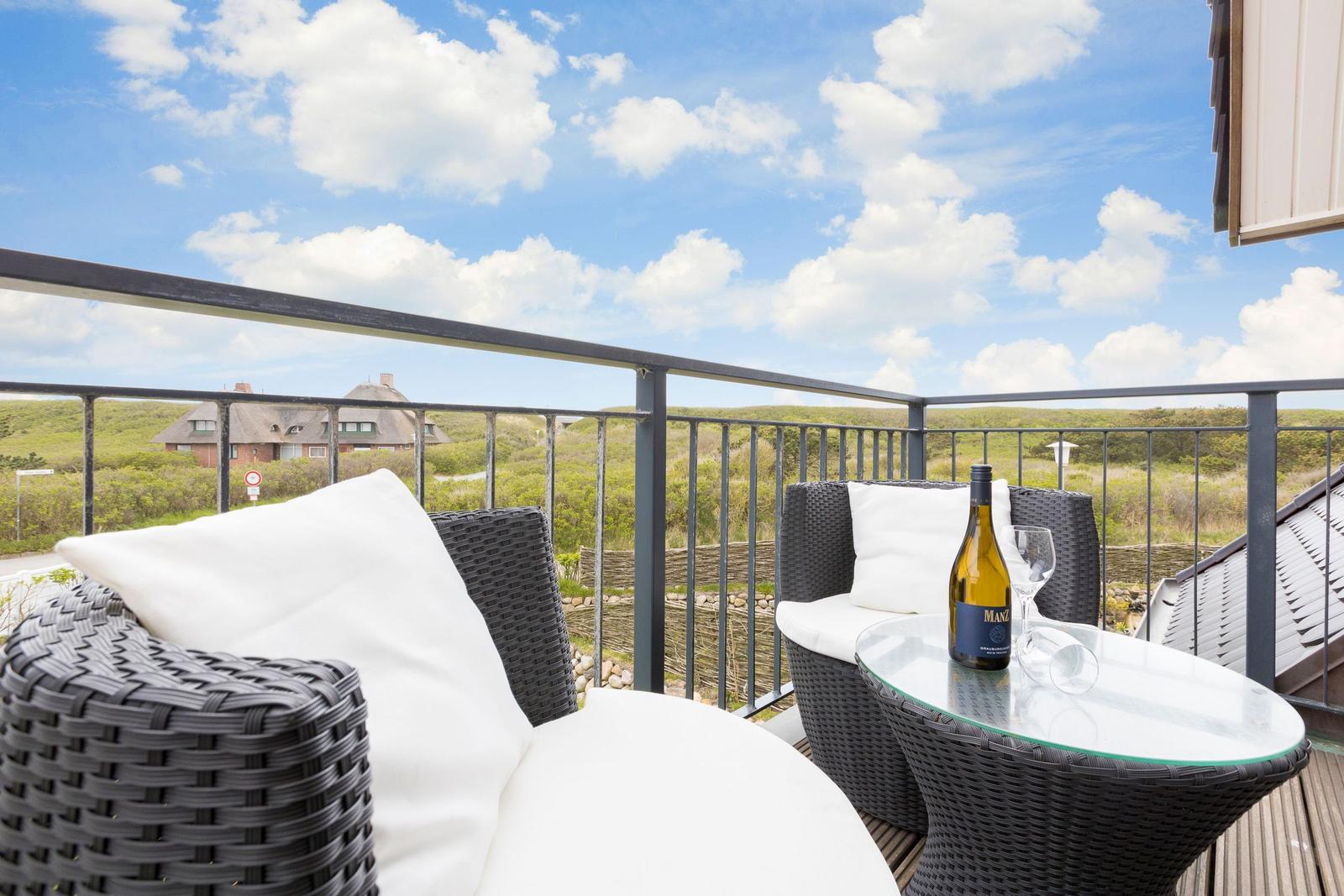 Terrasse mit zwei Sesseln, Tisch und Weinflasche. Blick auf grüne Landschaft und Haus.
