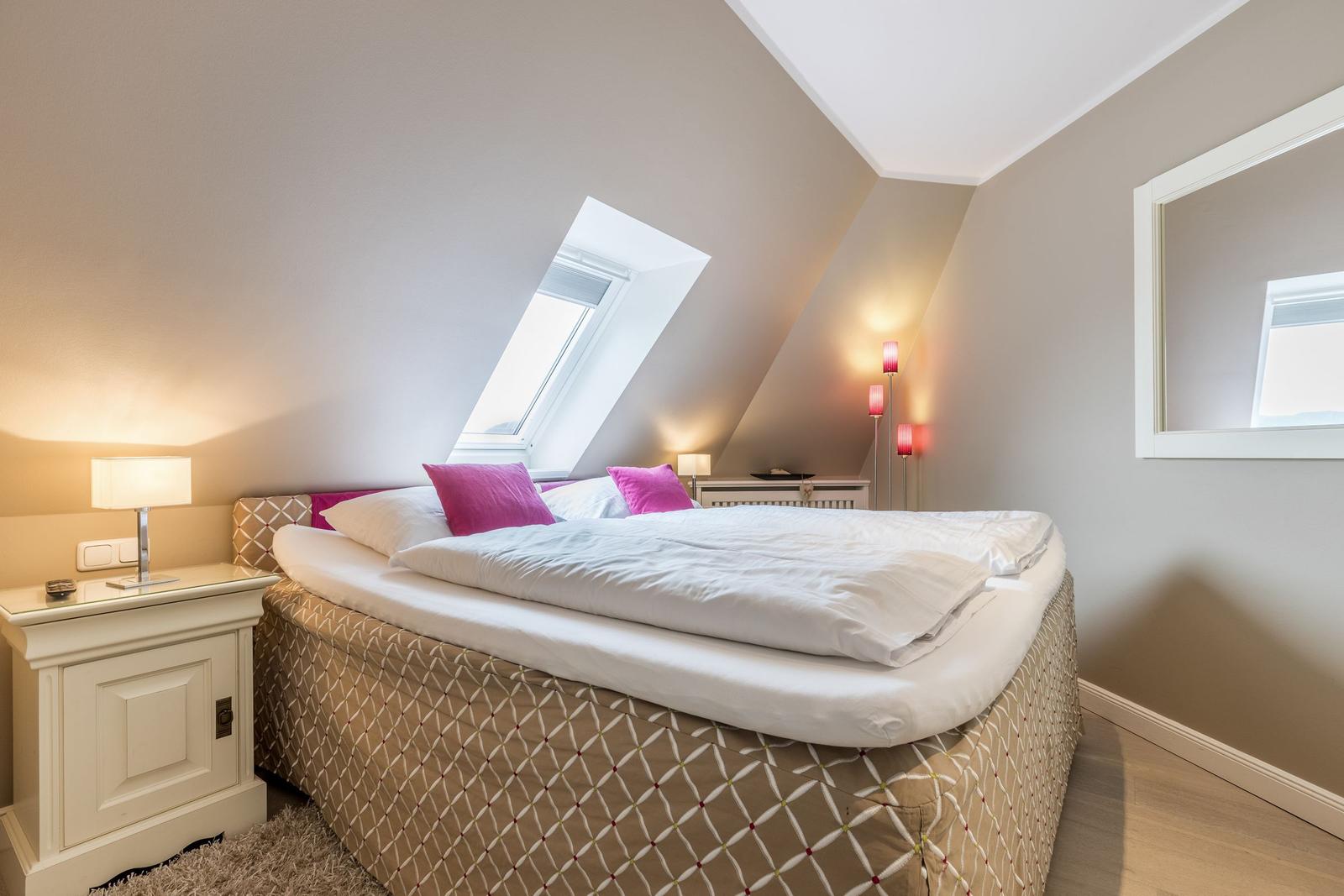Schlafzimmer mit Dachschrägen, Dachfenster und Bett mit rosa Kissen.
