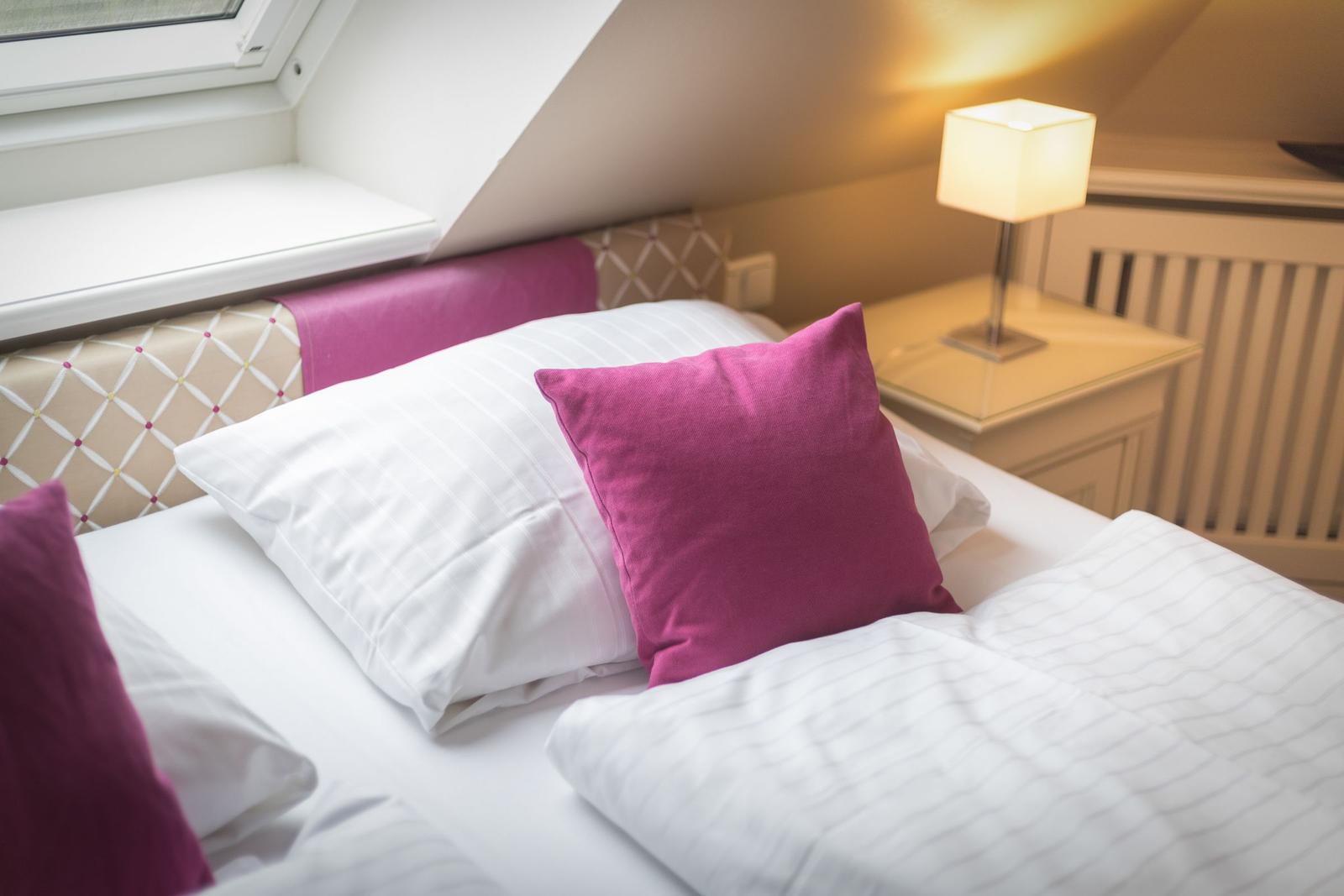 Schlafzimmer mit Bett, Kissen und Nachttisch unter Dachschrägen.