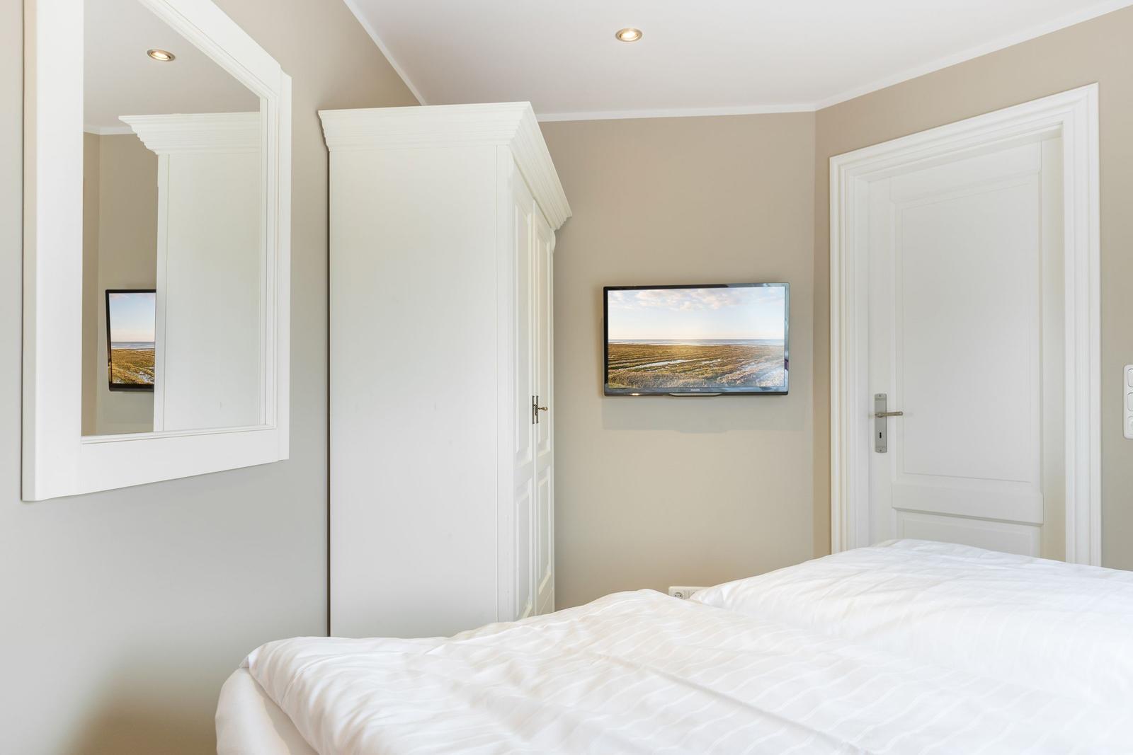 Schlafzimmer mit Bett, Spiegel, Kleiderschrank und Wandfernseher.