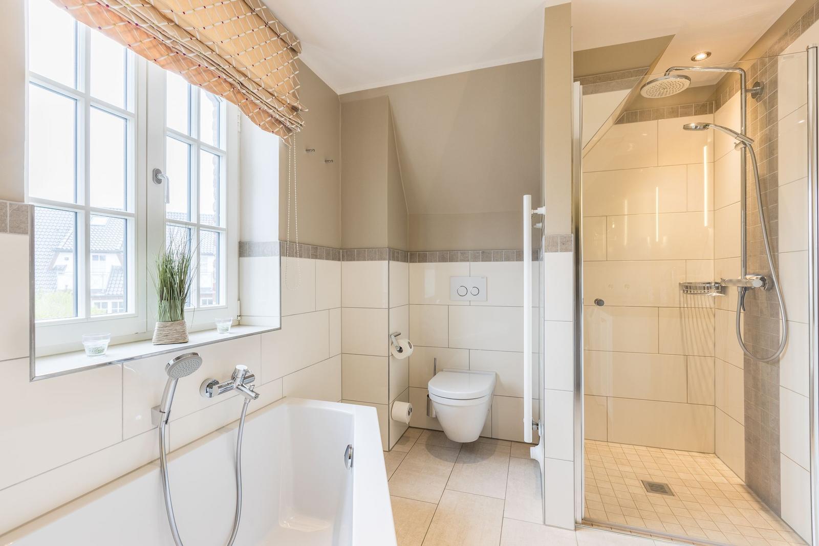 Badezimmer mit Badewanne, Dusche und Toilette. Fenster mit Pflanze.