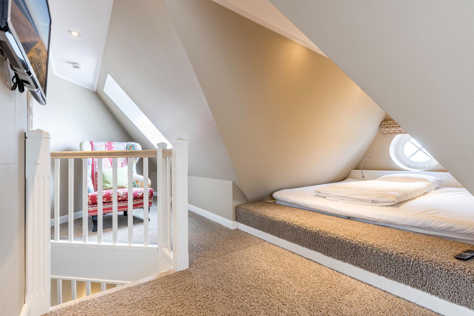 Schlafzimmer mit Dachschräge, Bett, Fenster und Sitzgelegenheit.