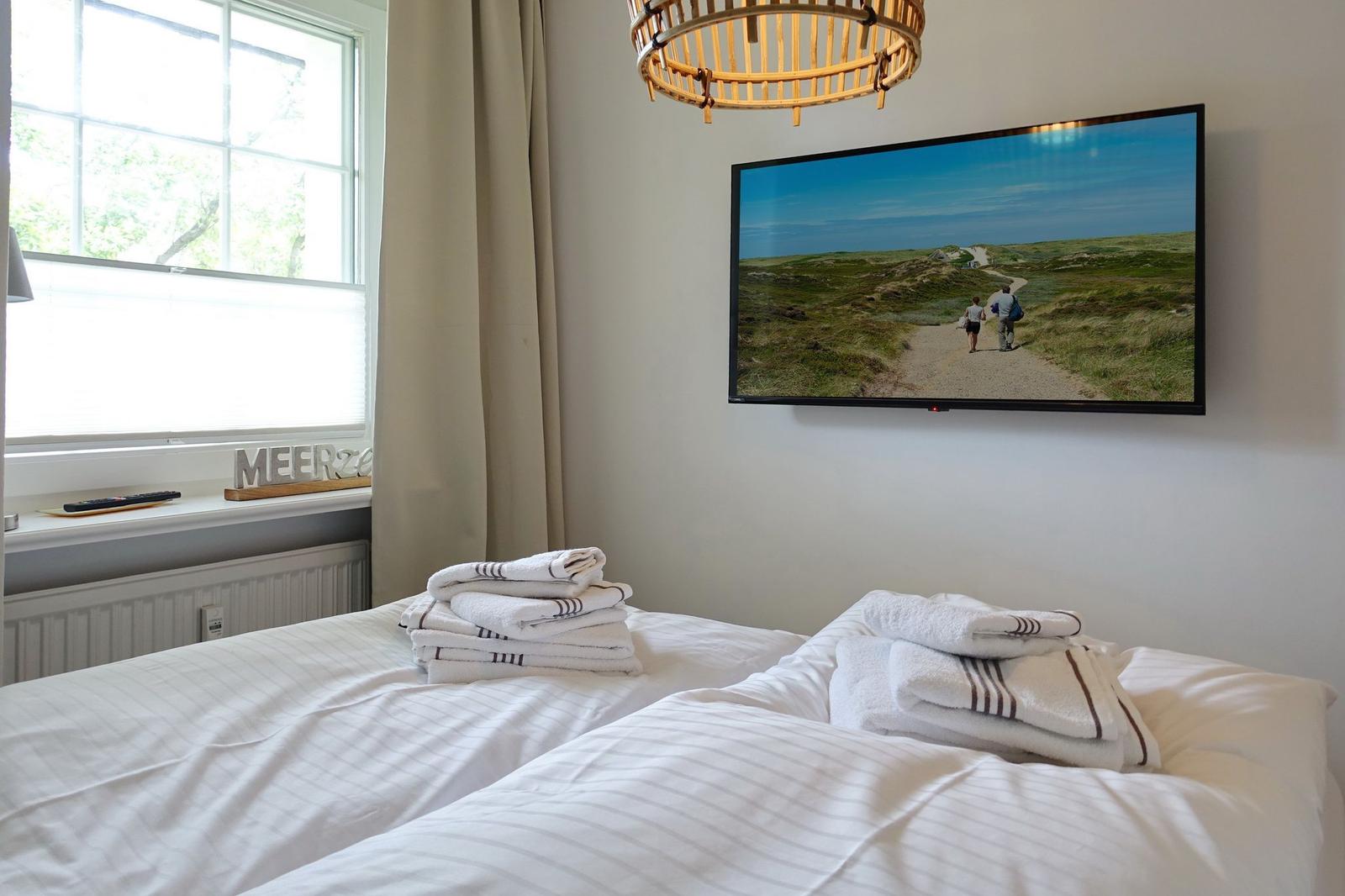 Room with bed, TV, and window. Towels on the bed.