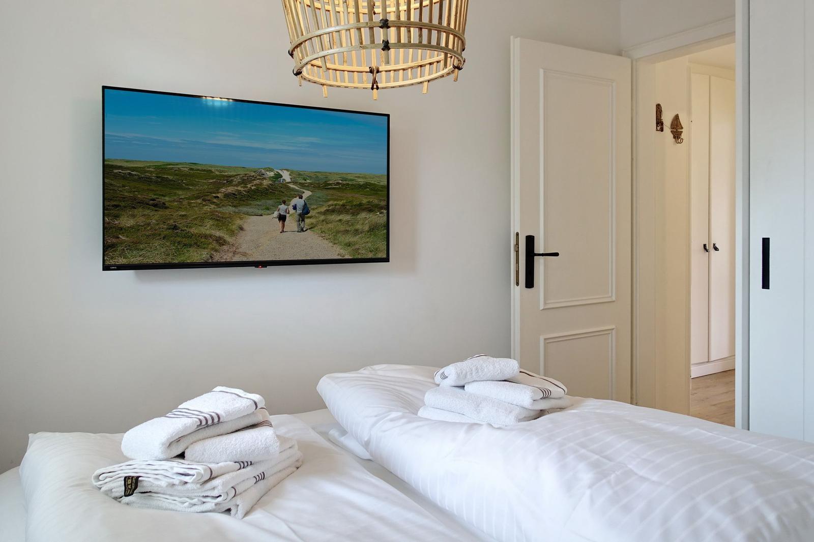 Bedroom with bed, towels, and wall picture. Ceiling and door visible.