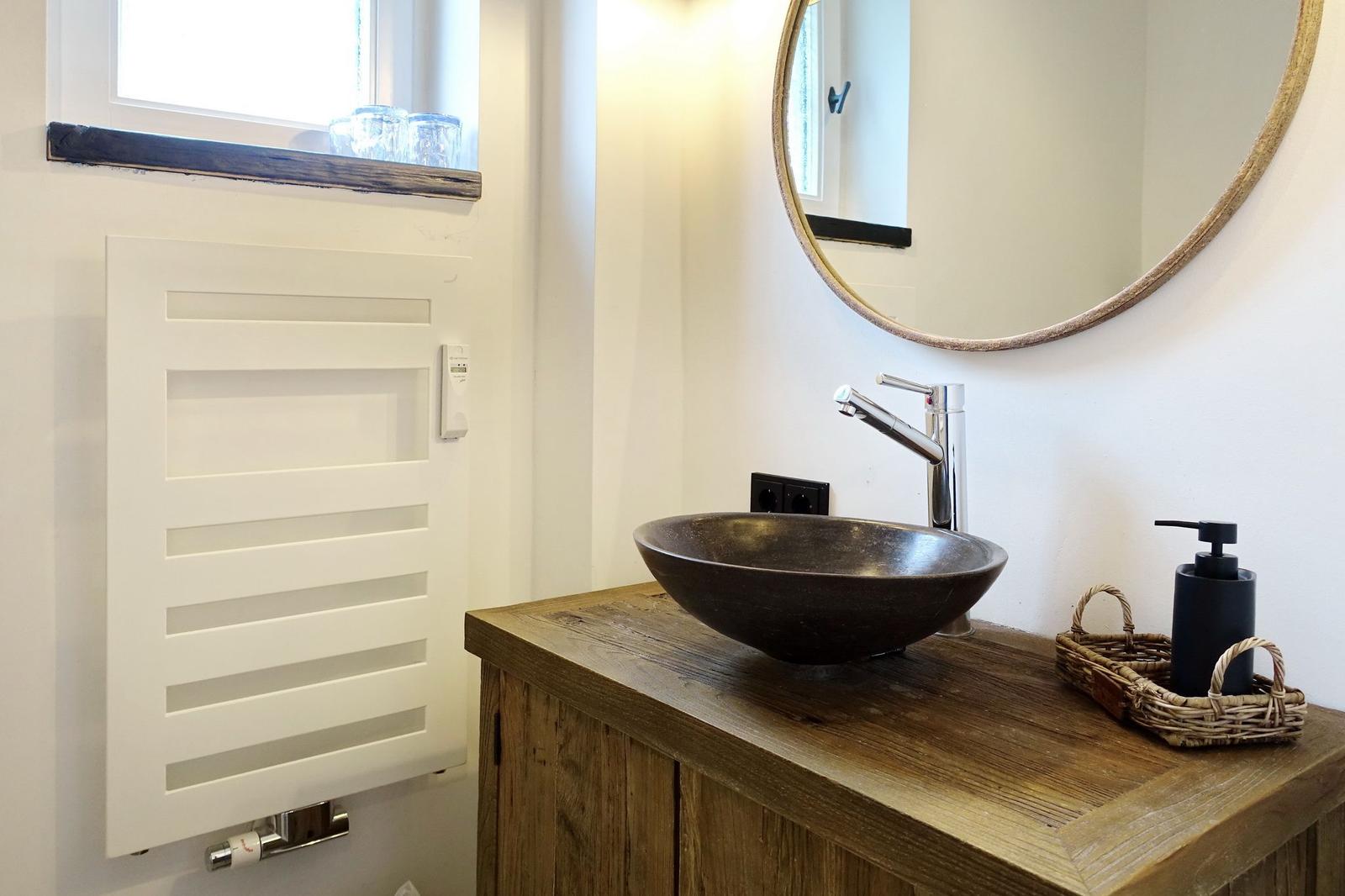 Bathroom with wooden vanity, round mirror, and heater.