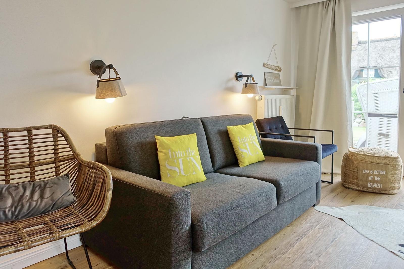 Gray sofa with yellow cushions, rattan chair, and garden view through window.