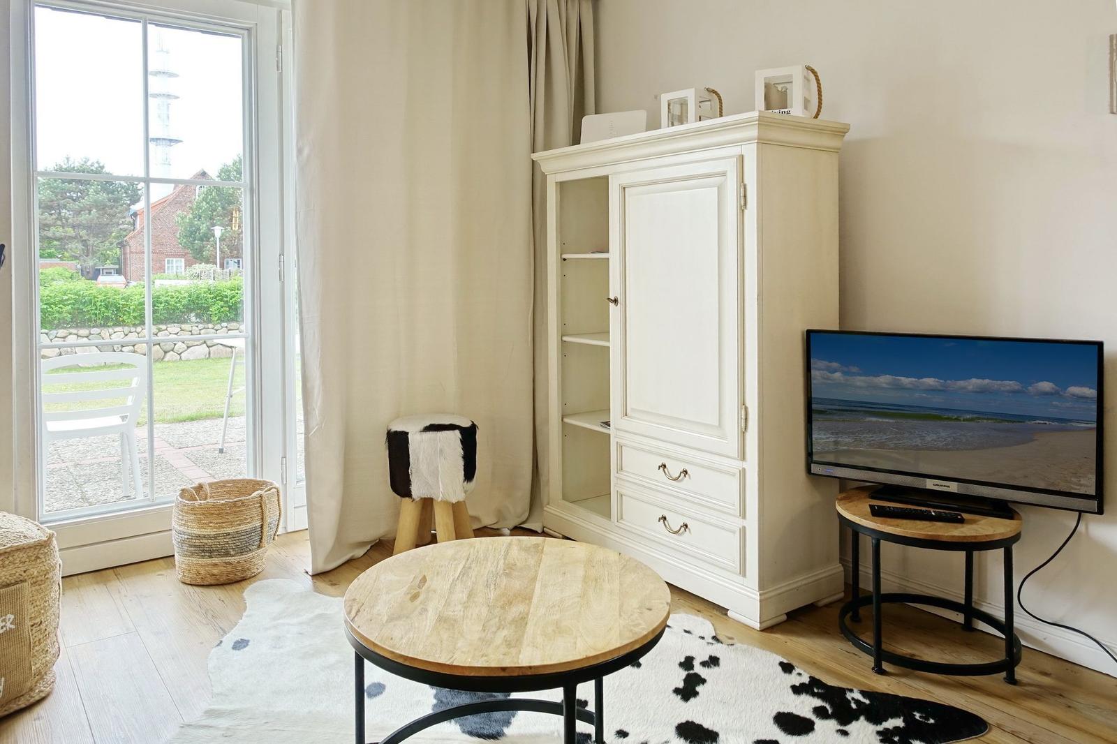 Living room with TV, cabinet, and table. Entrance to terrace with view of garden.