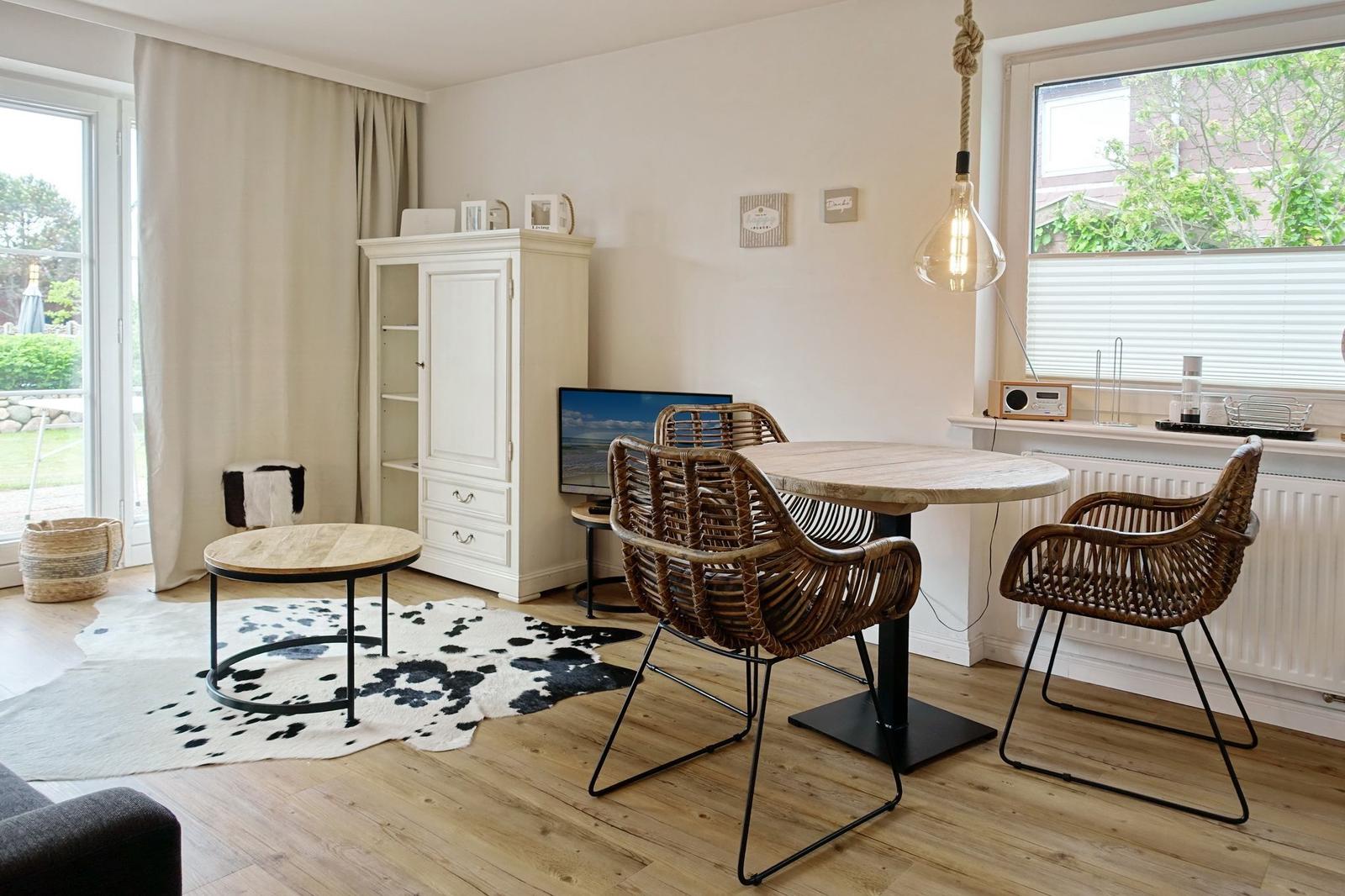 Dining room with round table, chairs, and TV. Windows, curtains, and wooden floor.