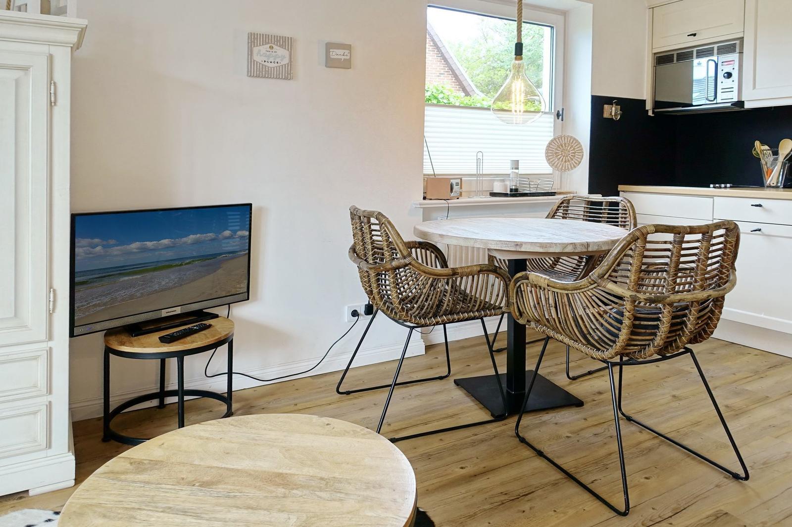 Dining room with round table, chairs, and TV. Wooden floor and window with blinds.