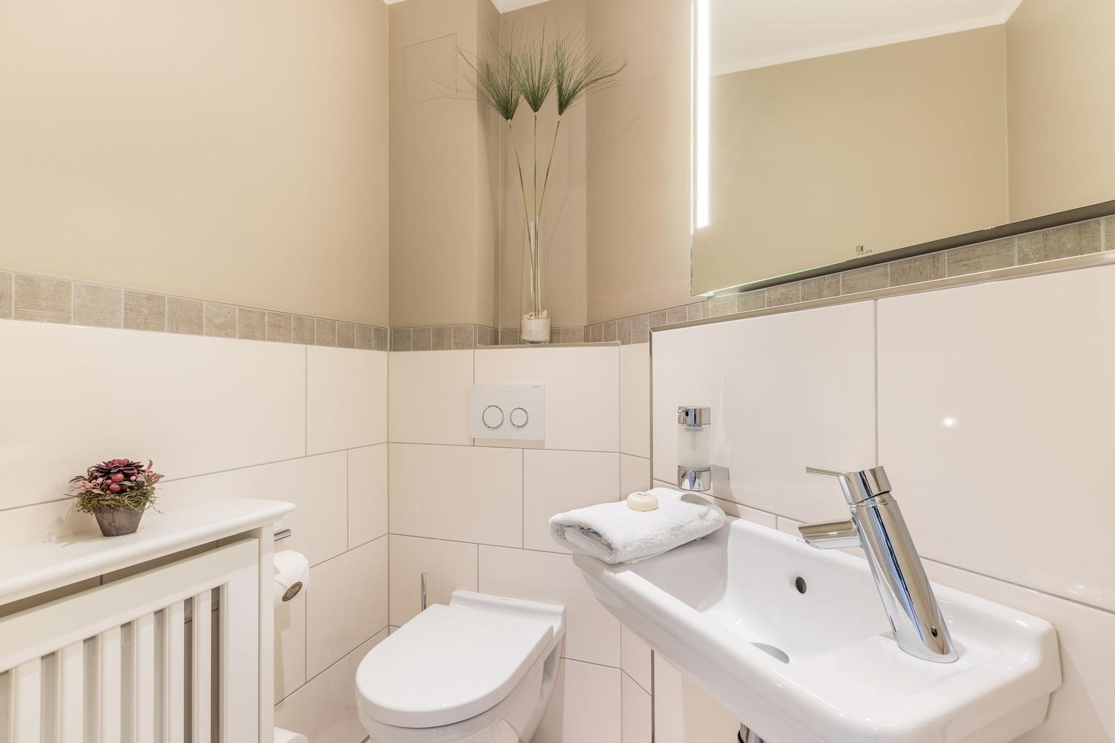 Badezimmer mit Toilette, Waschbecken und Spiegel. Dekorative Pflanzen und Handtuch.