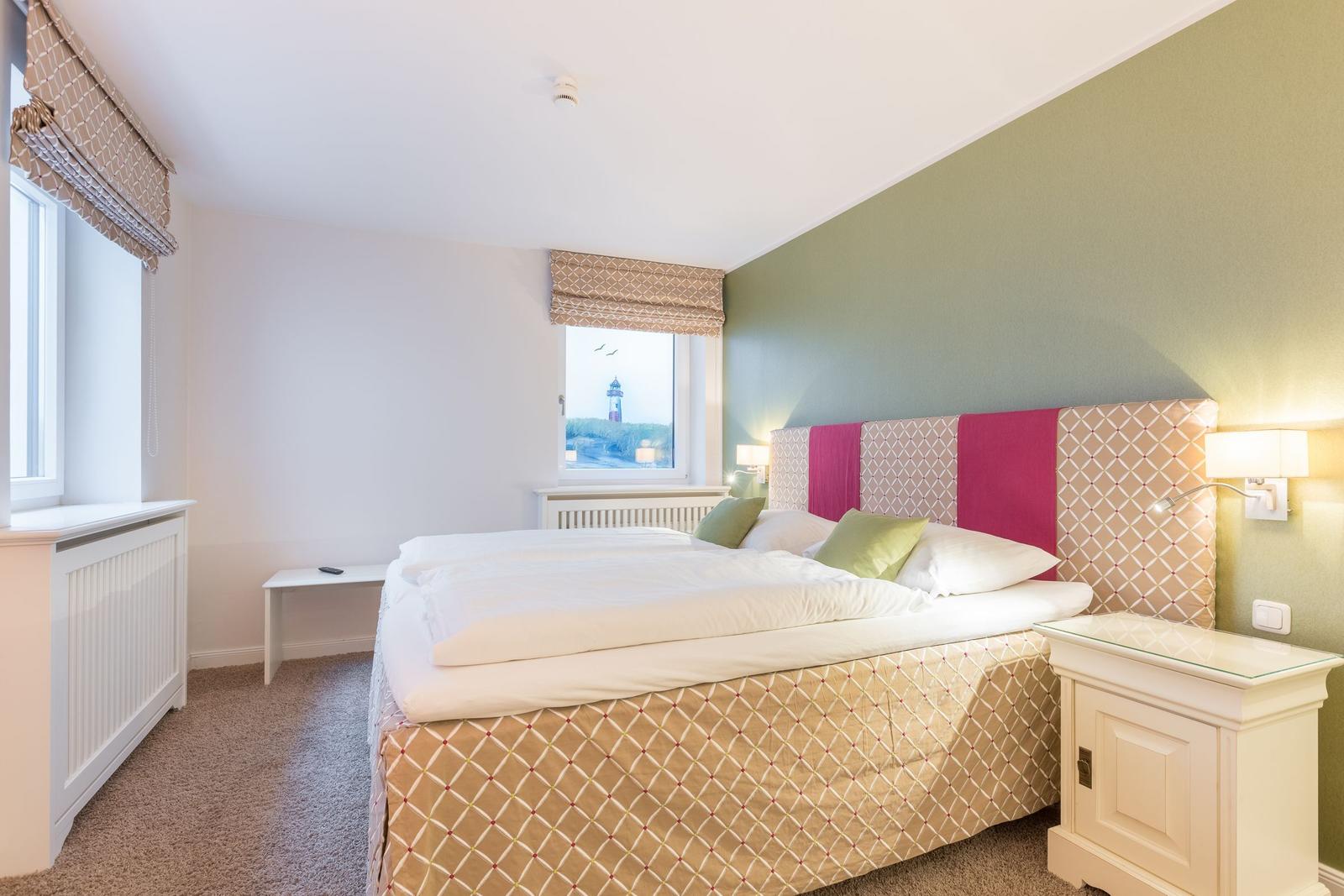 Schlafzimmer mit Bett, Nachttisch und Fenster zum Leuchtturm