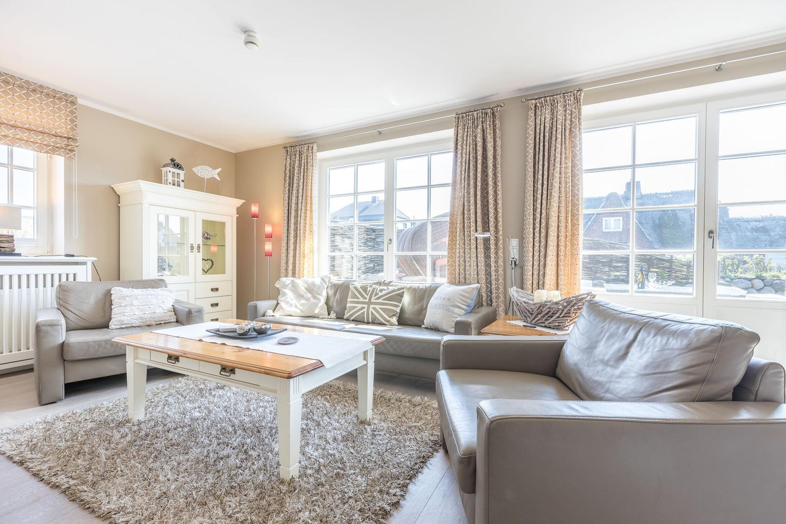 Wohnzimmer mit Sofa, Sessel und Tisch. Große Fenster mit Blick nach draußen.