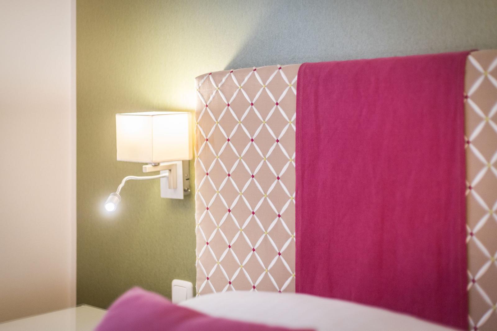 Bettkopfteil mit rosa Decke und Wandlampe.