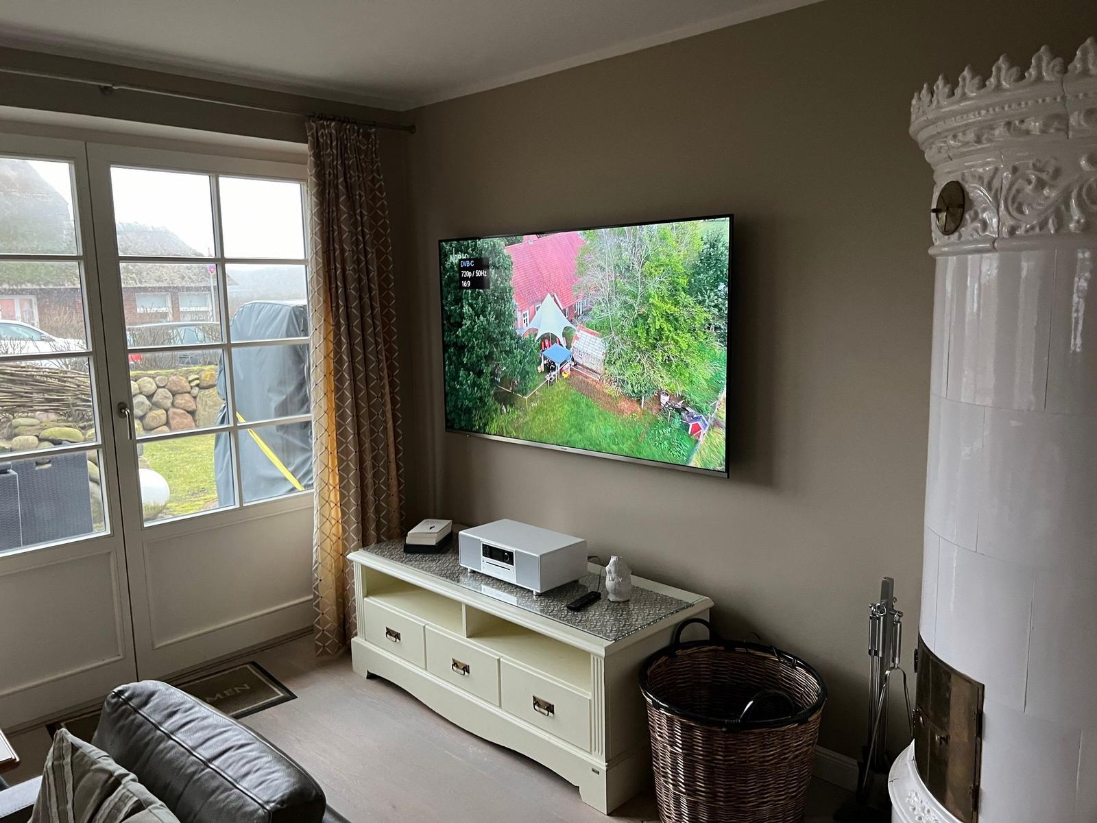Wohnzimmer mit Fernseher, Kamin und Blick auf den Garten.