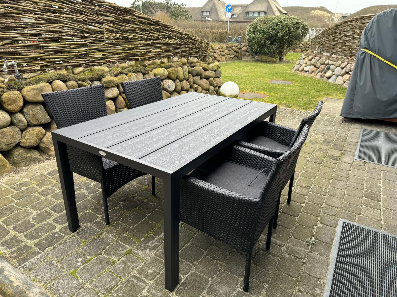 Gartenmöbel mit Tisch und vier Stühlen auf Steinplatten.