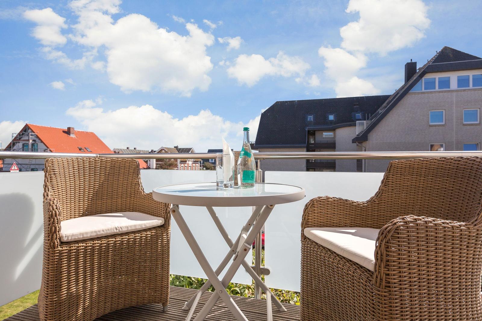 Terrasse mit zwei Stühlen und Tisch. Im Hintergrund sind Gebäude und Himmel zu sehen.
