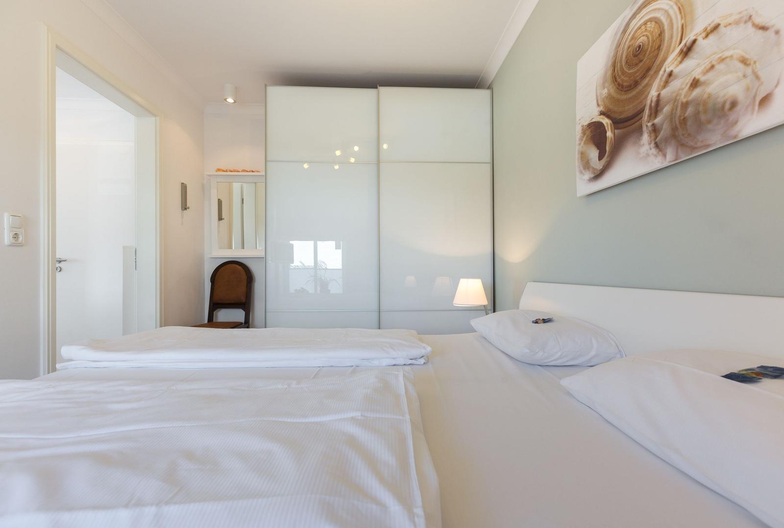 Schlafzimmer mit weißem Bett, Kleiderschrank und Wandbild.