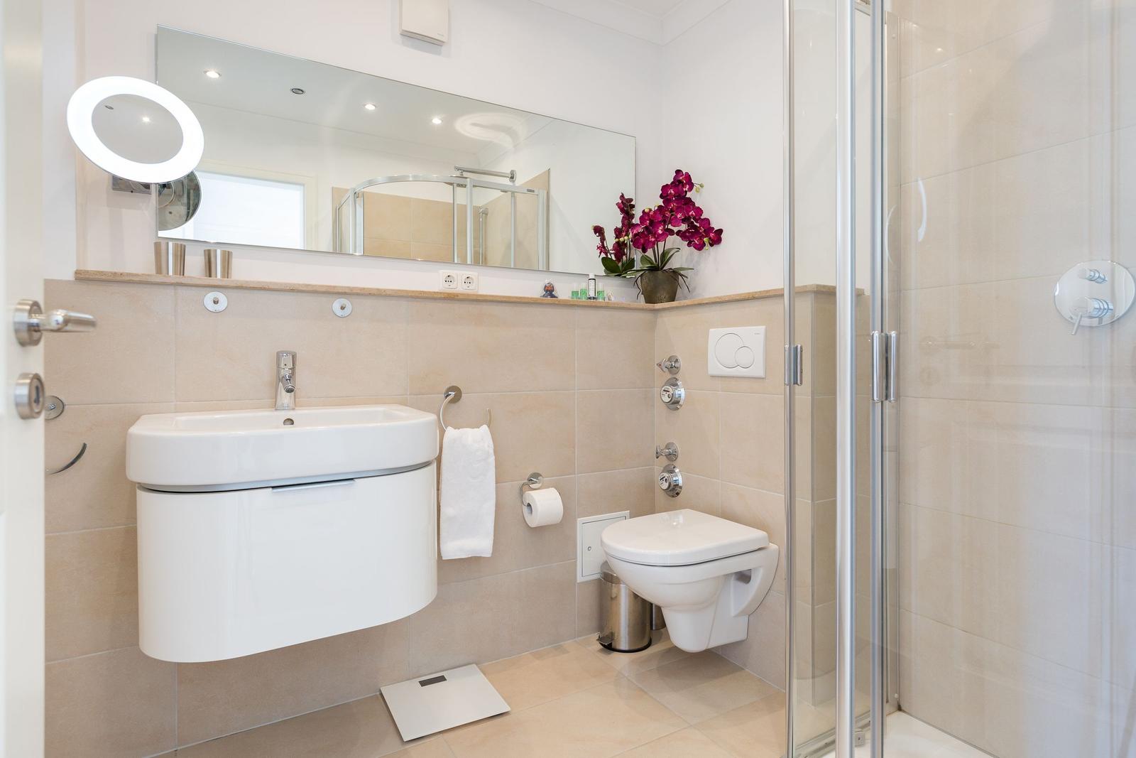 Badezimmer mit Dusche, Waschbecken und Toilette. Mit Spiegel und Orchidee.