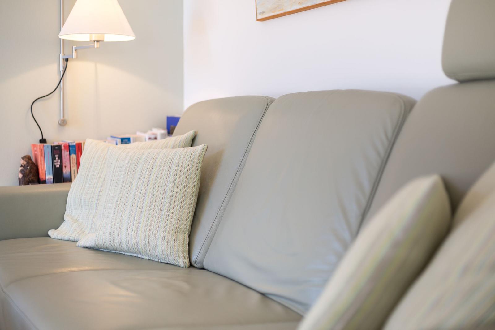 Ein grauer Ledersofa mit Kissen und einer Wandlampe im Hintergrund.