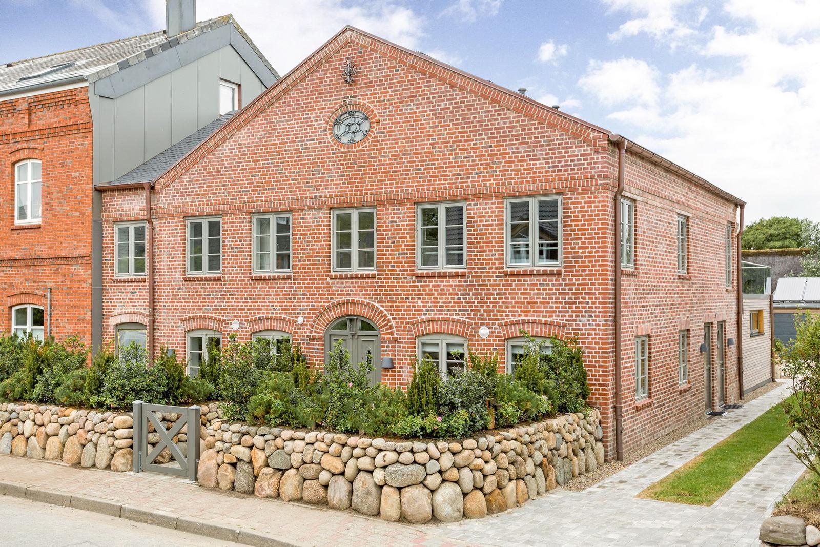 Red brick building with stone wall and green garden border.