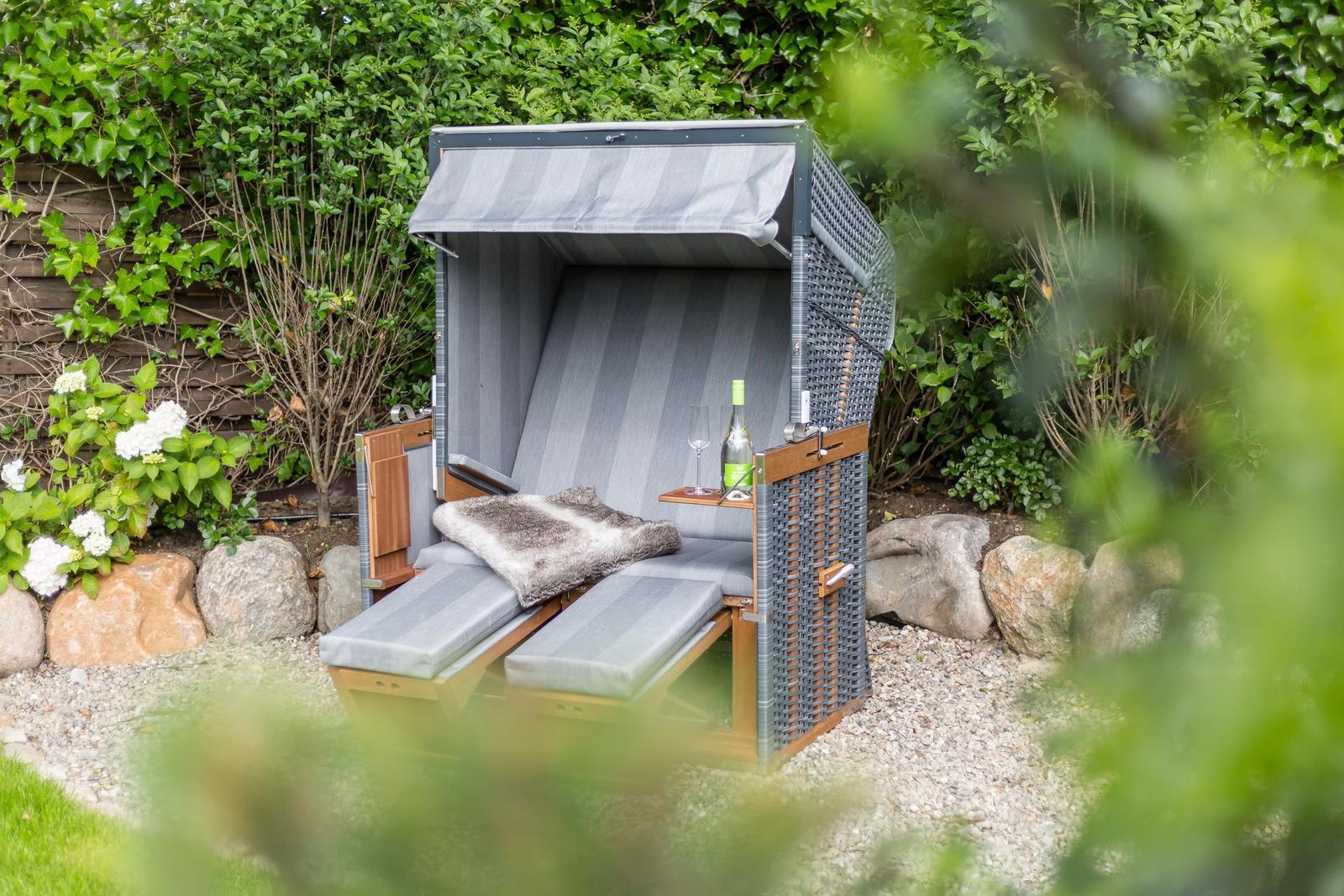 Garden lounger with canopy, drink, and fur blanket between shrubs and stones
