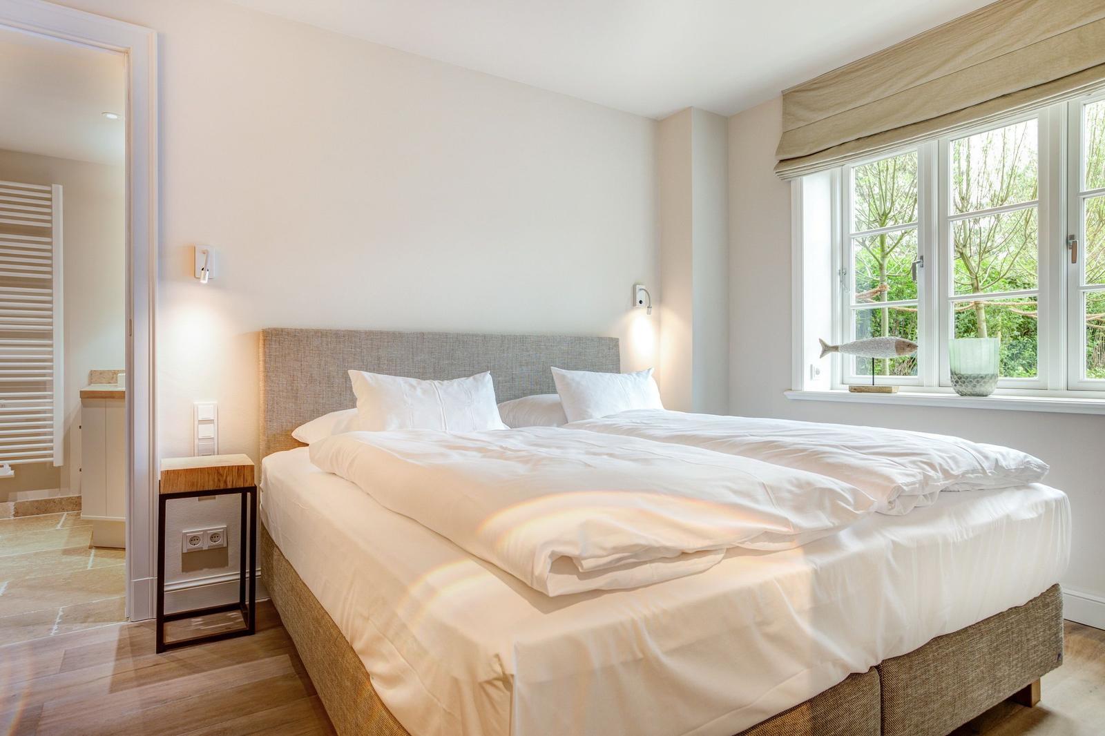 Bedroom with double bed, window, and view of greenery. Adjacent room with heater.