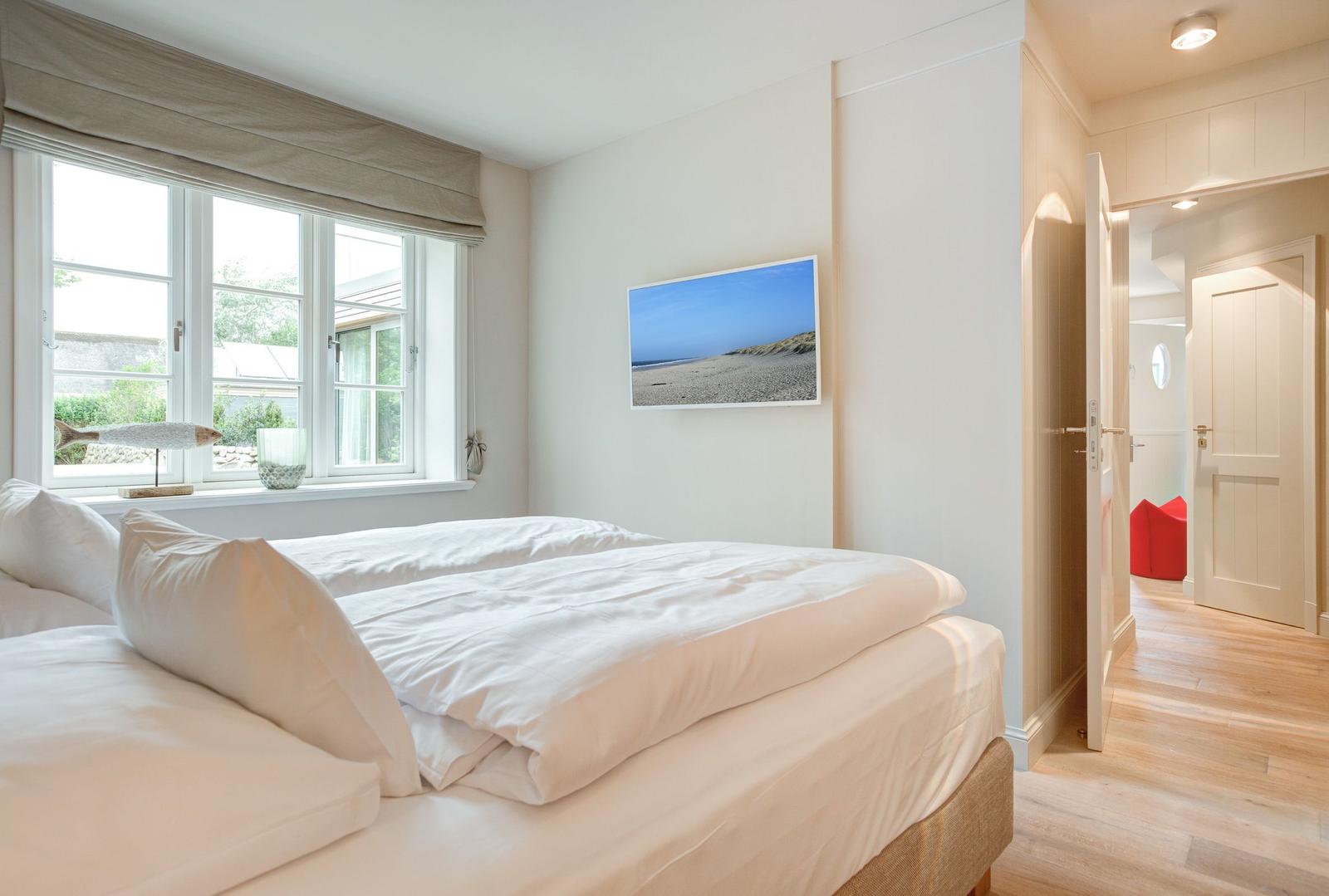 Bedroom with bed, window, and wall picture. Corridor to adjacent rooms.