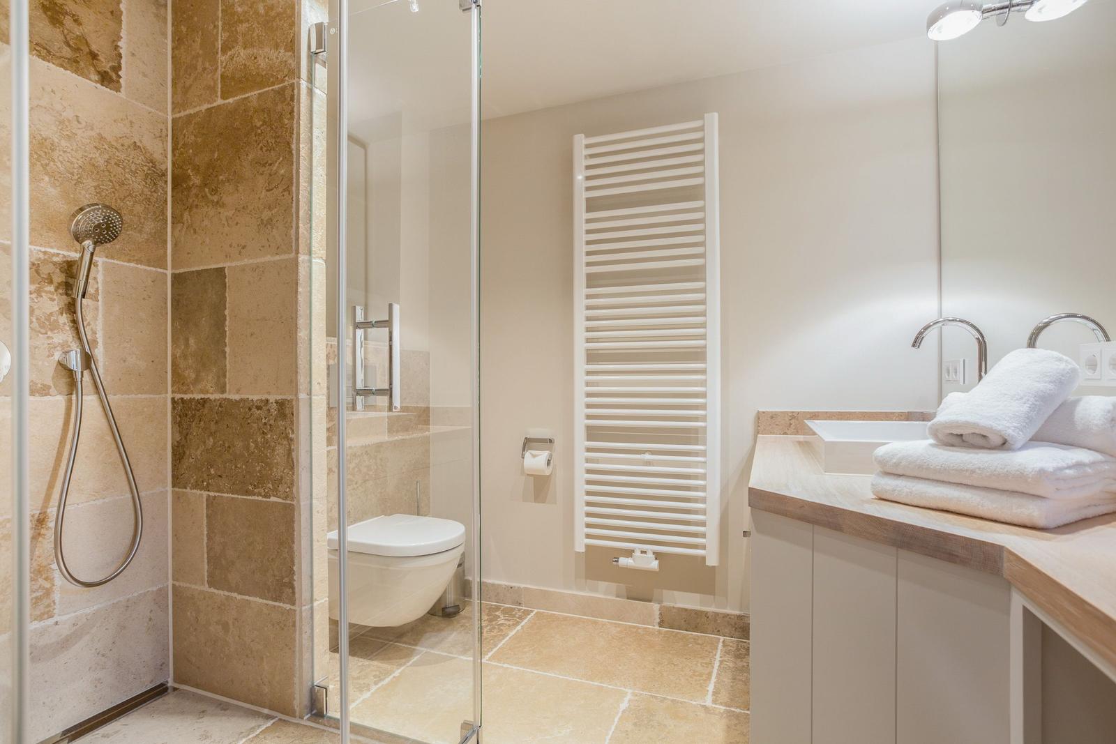 Shower with stone wall, toilet and sink with towels