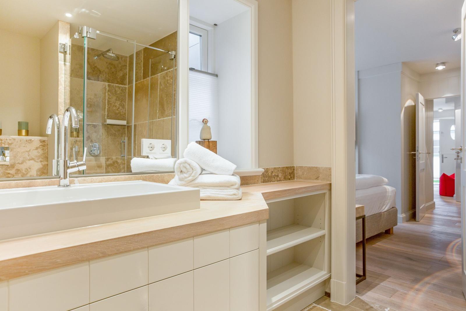Bathroom with shower, sink, and towels. View into the bedroom.