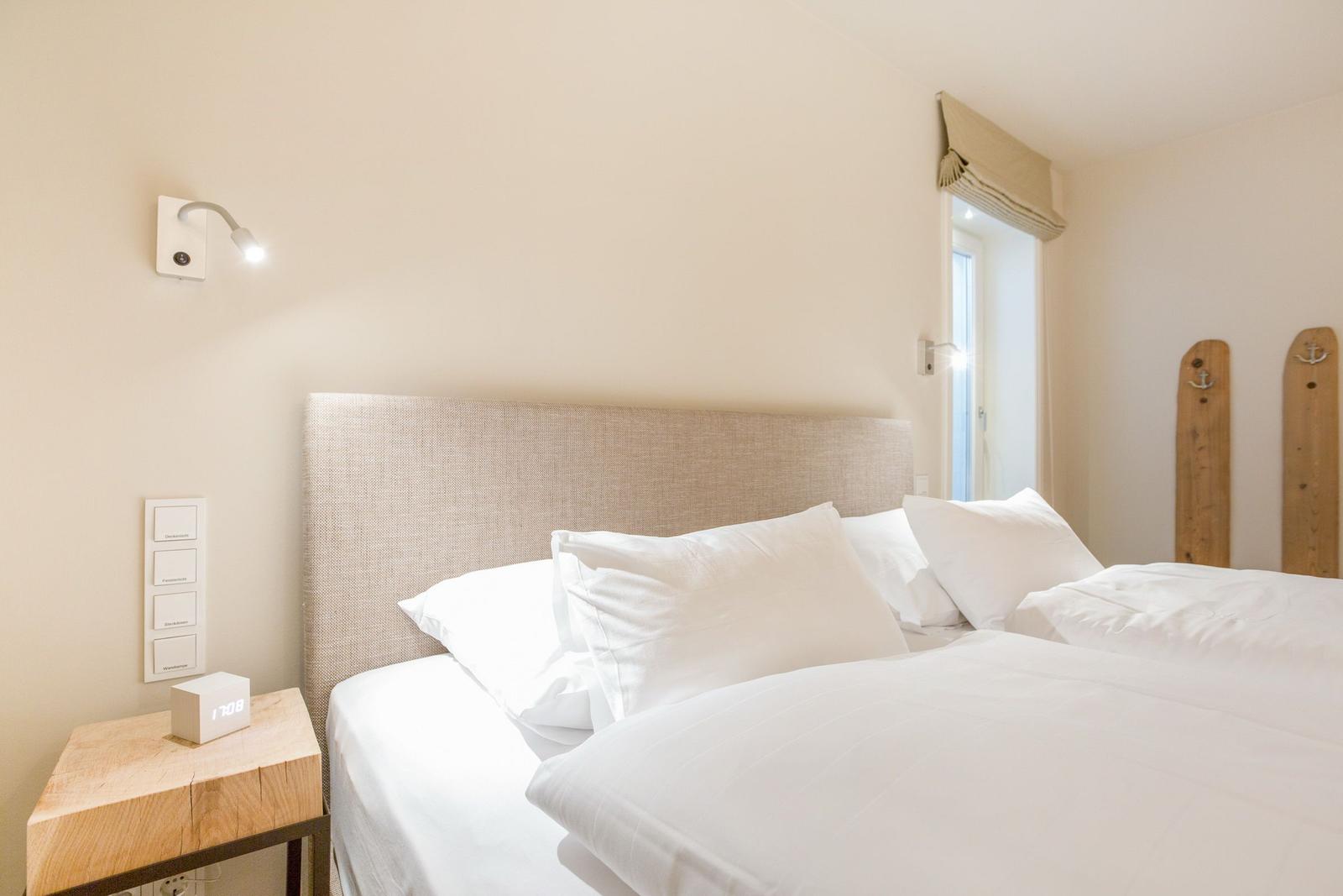 Bedroom with bed, nightstand, and wall lamp. Window and wooden panels visible.