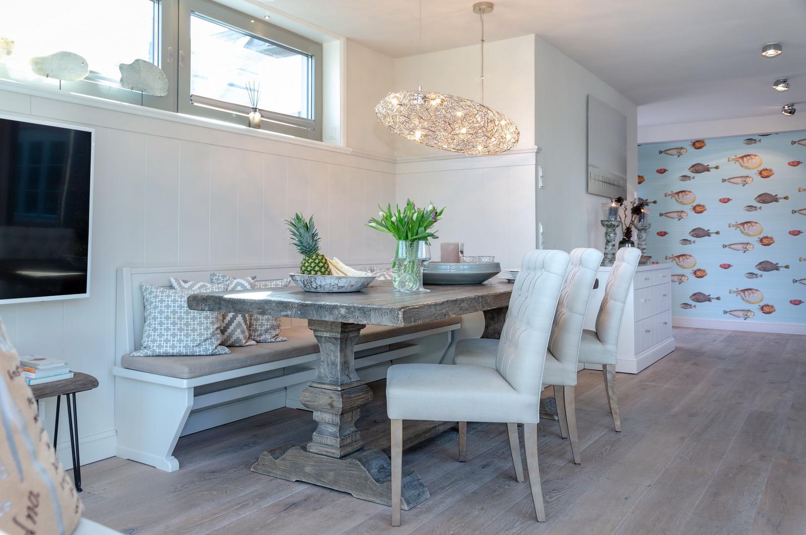 Dining room with wooden table, bench, and chairs. Wall with fish motif. Ceiling light and windows.