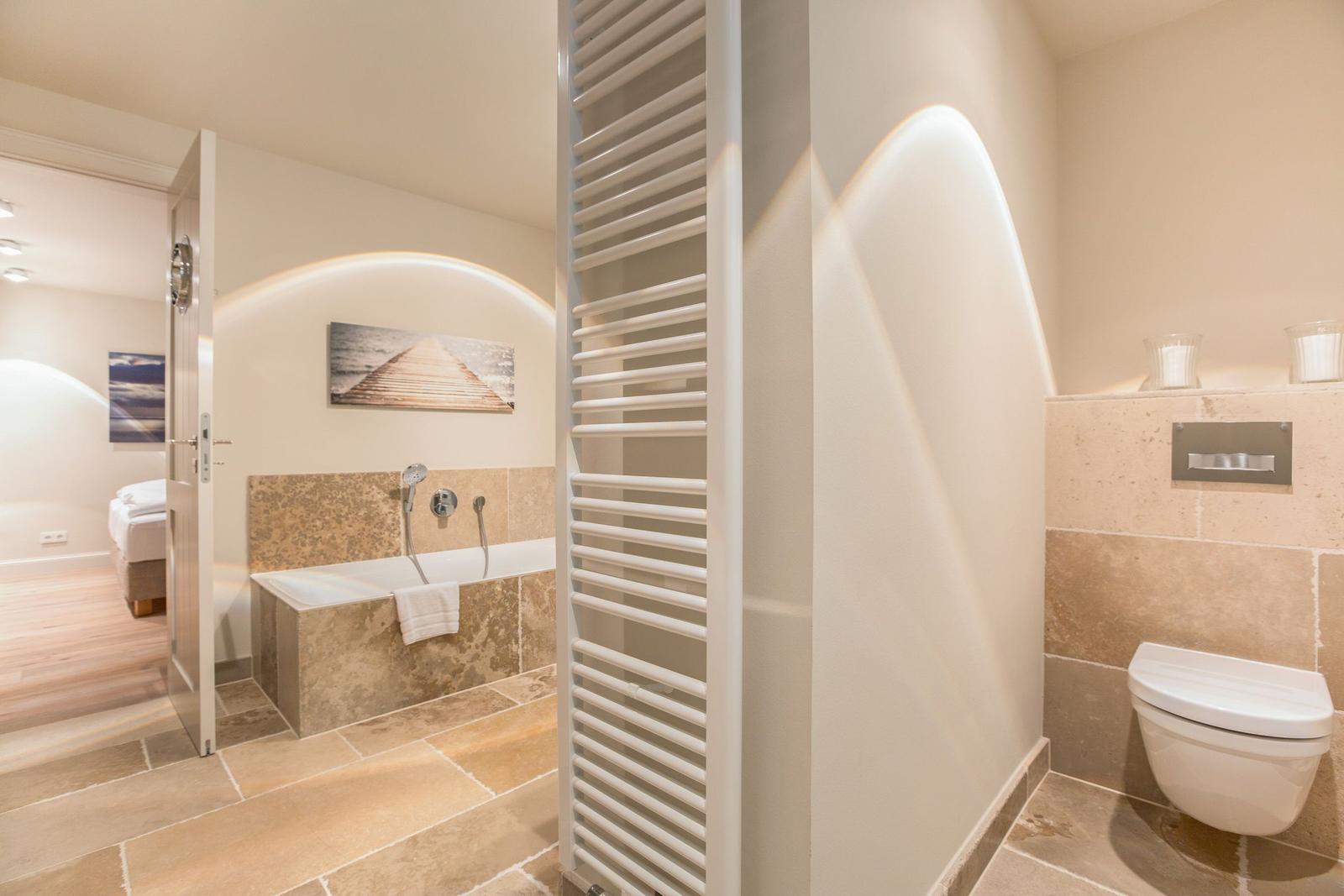 Bath with bathtub, toilet, and heater. Door leads to bedroom.
