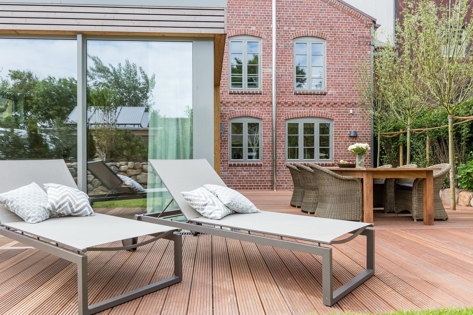 Deck with loungers, table and chairs in front of brick house